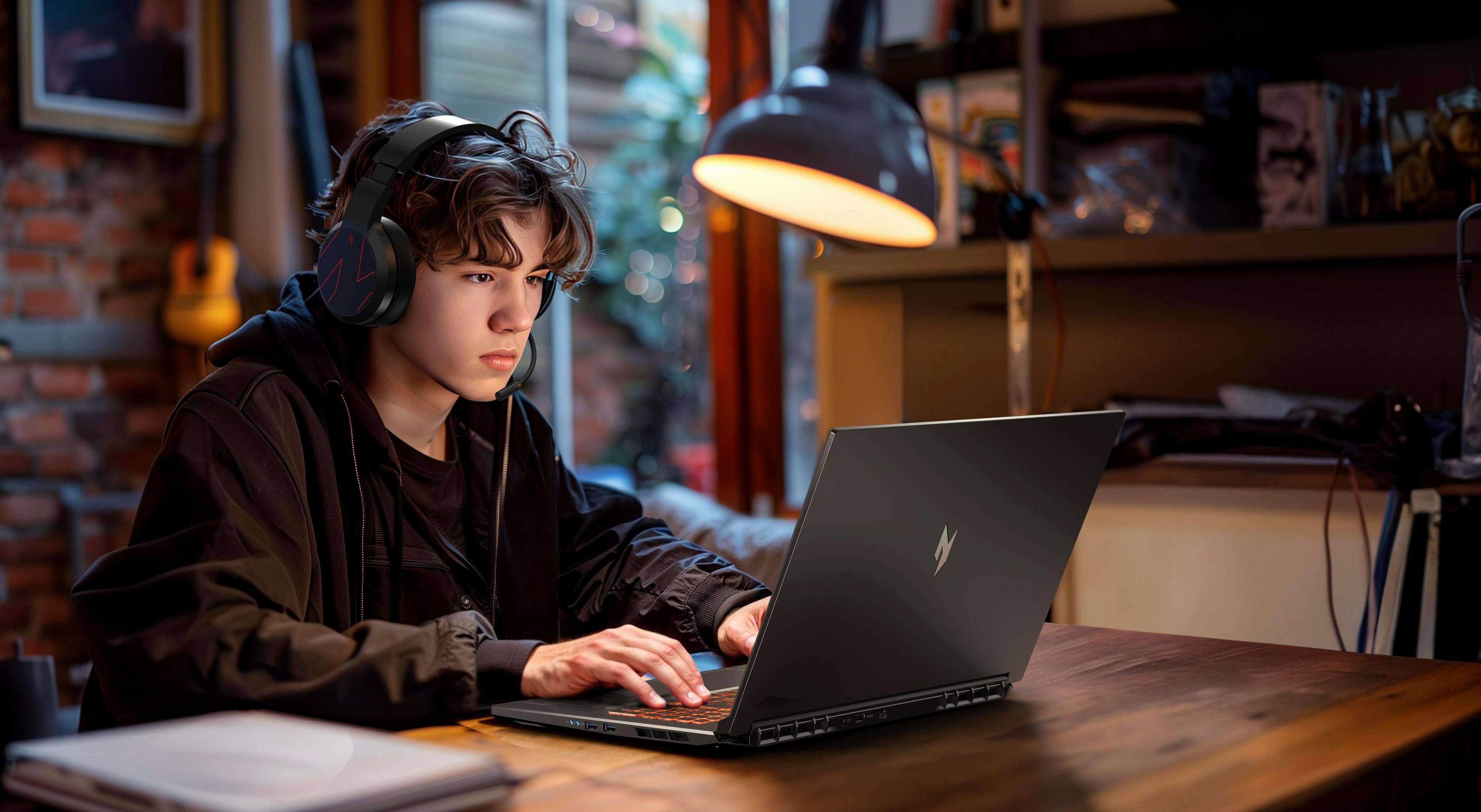 Ein junger Mann mit Kopfhörern, der einen Laptop benutzt, spielt. Der Laptop steht auf einem Holztisch.