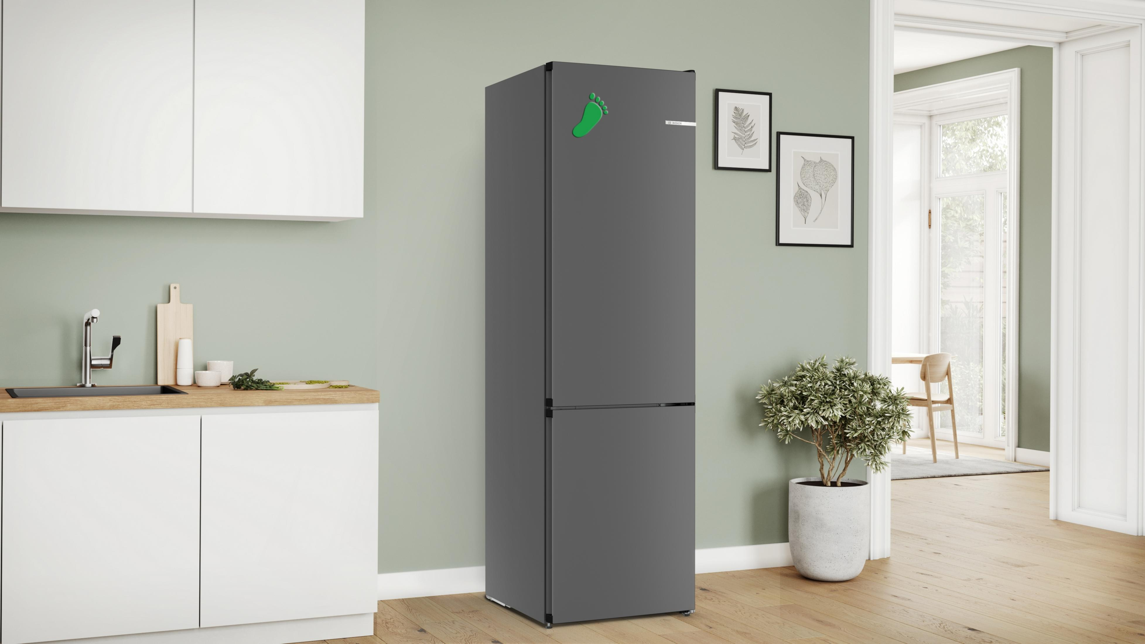 Ein grauer Kühlschrank in einer Küche mit einem grünen Fußabdruck-Aufkleber und einer Pflanze davor.
