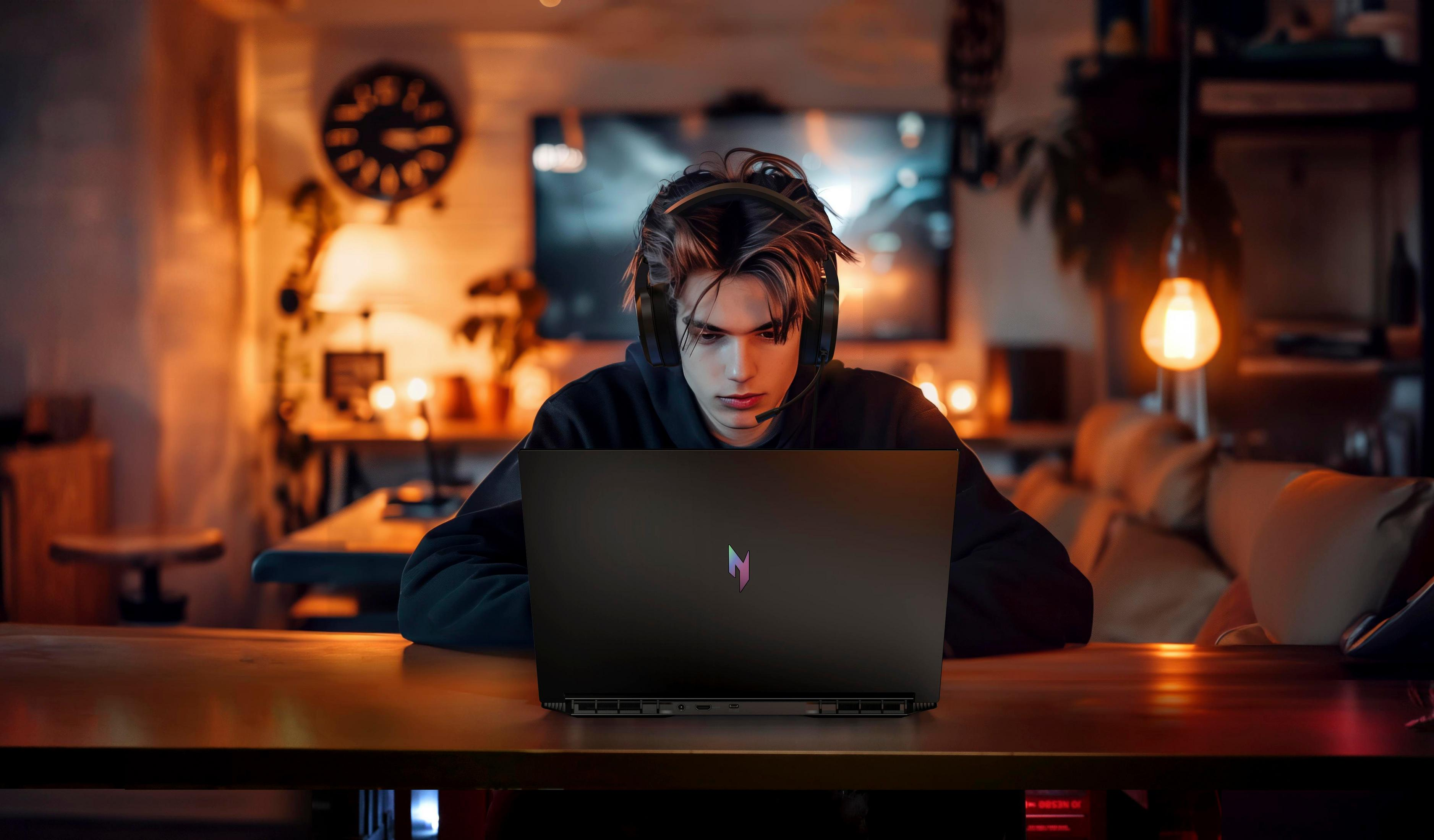 Ein junger Mann mit Kopfhörern, der auf einen Laptop-Bildschirm blickt, beleuchtet von einer Lampe.