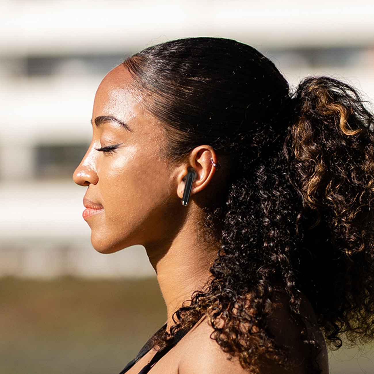 Kobieta z kręconymi włosami nosi czarną słuchawkę w uchu, patrząc w lewo.