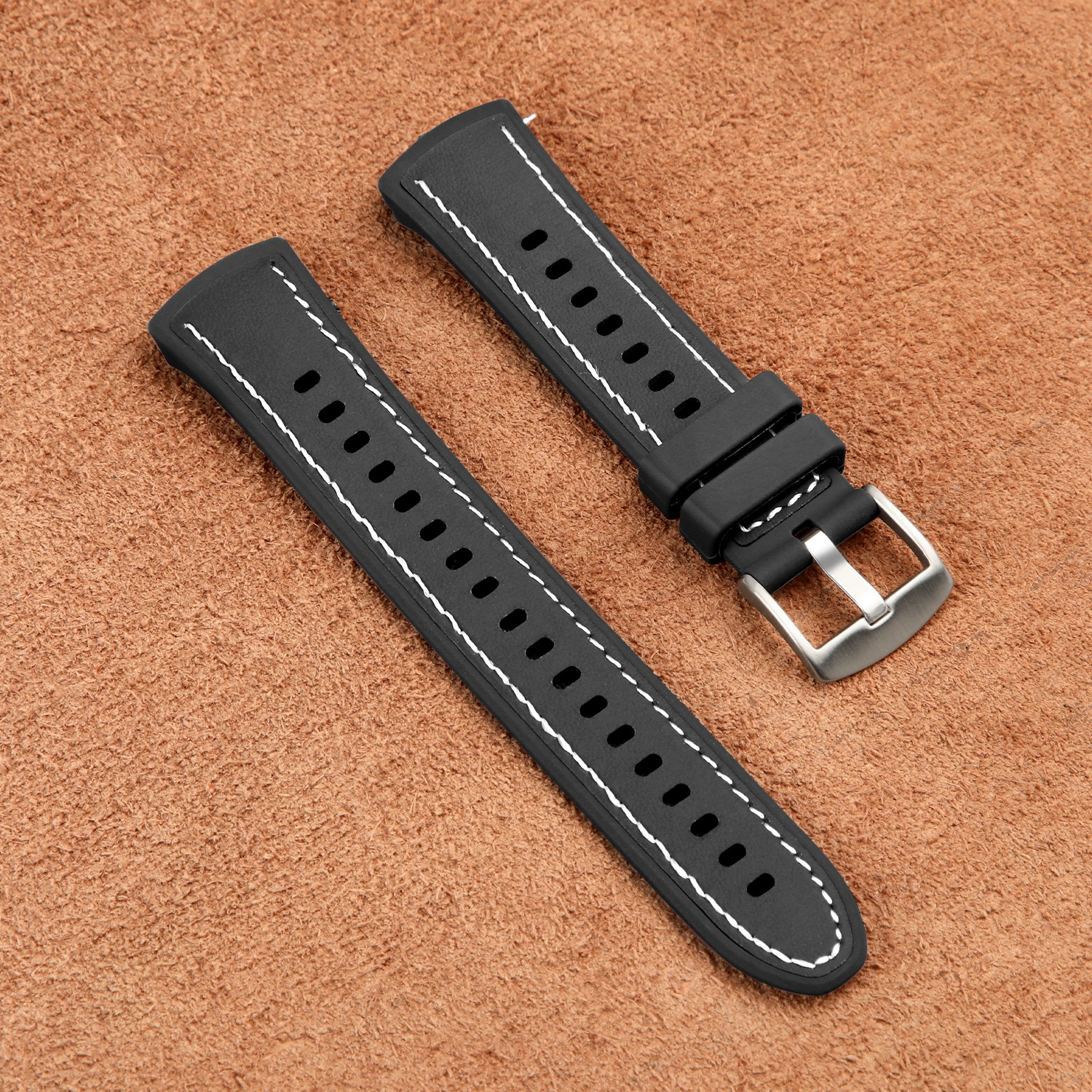 Zwei schwarze Uhrenarmbänder mit weißen Nähten, die auf einer braunen, strukturierten Oberfläche liegen.