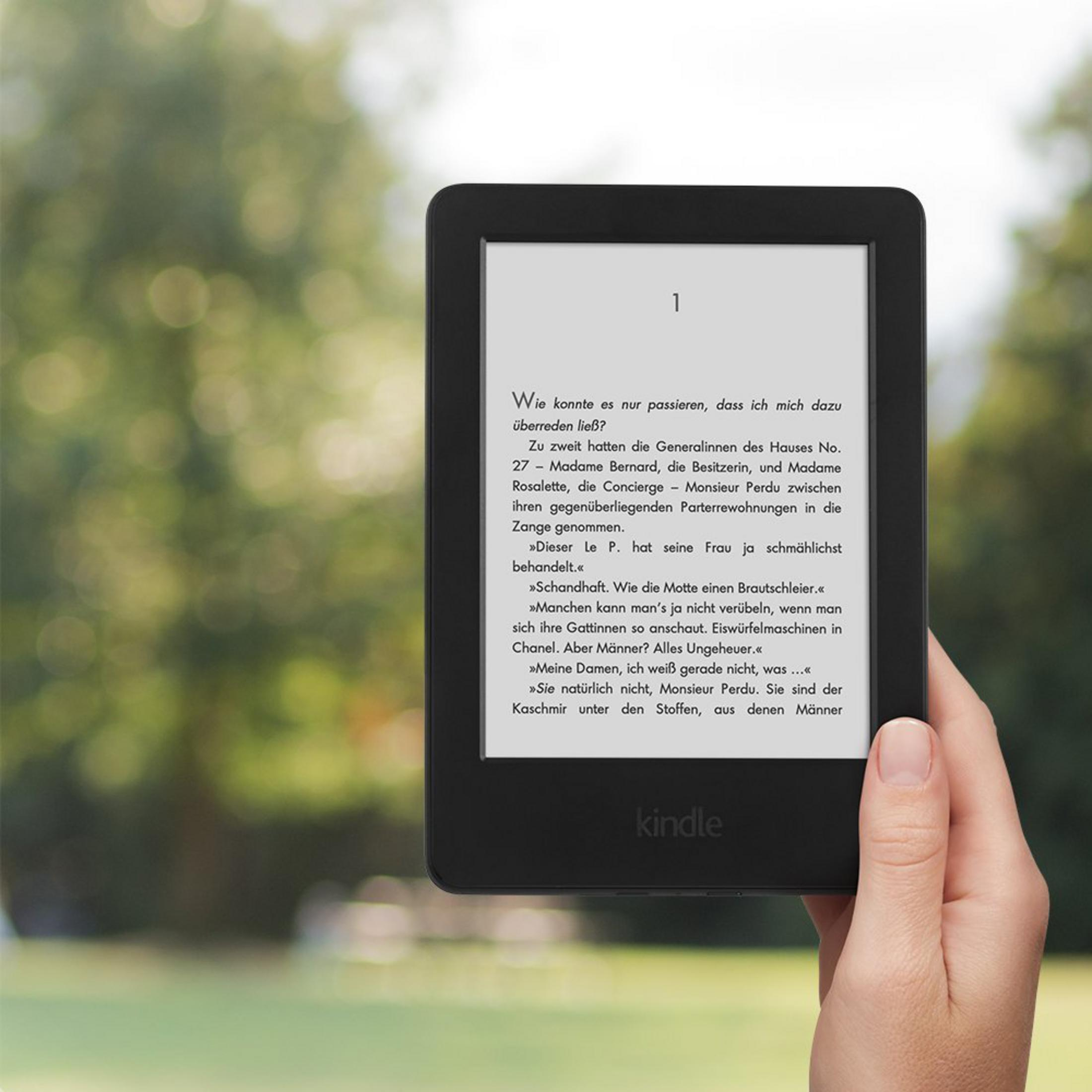 Hand hält einen Kindle E-Reader. Der E-Reader zeigt Text mit unscharfem Hintergrund.