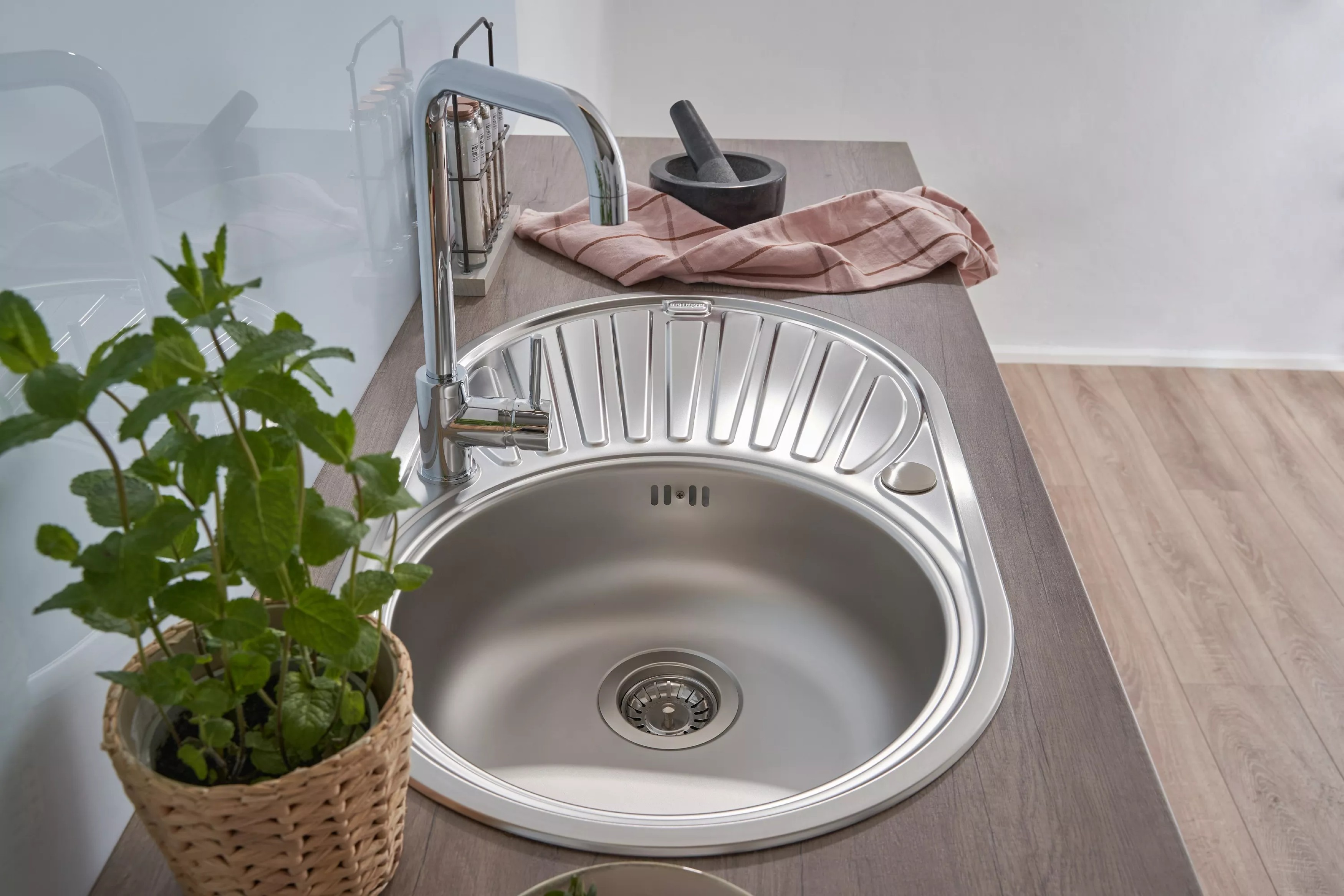 Ein Küchenbecken mit Wasserhahn, Minzpflanze und einem Marmor-Mörser und -Stößel auf einer Holz-Arbeitsplatte.