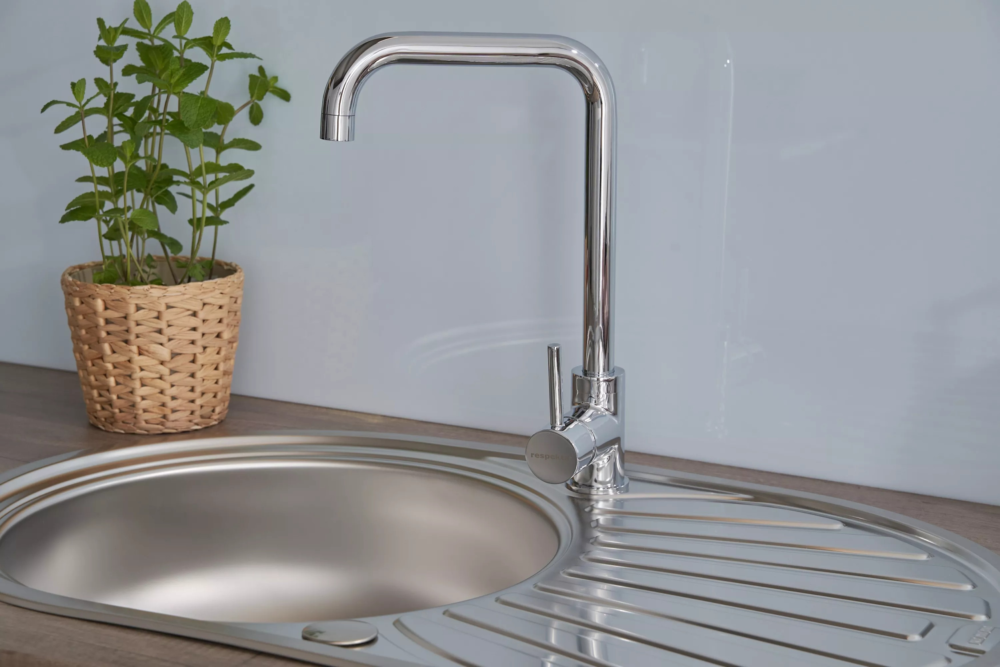 Nahaufnahme eines Küchenbeckens mit Wasserhahn und einem Topf mit Minze. Das Becken ist Edelstahl.