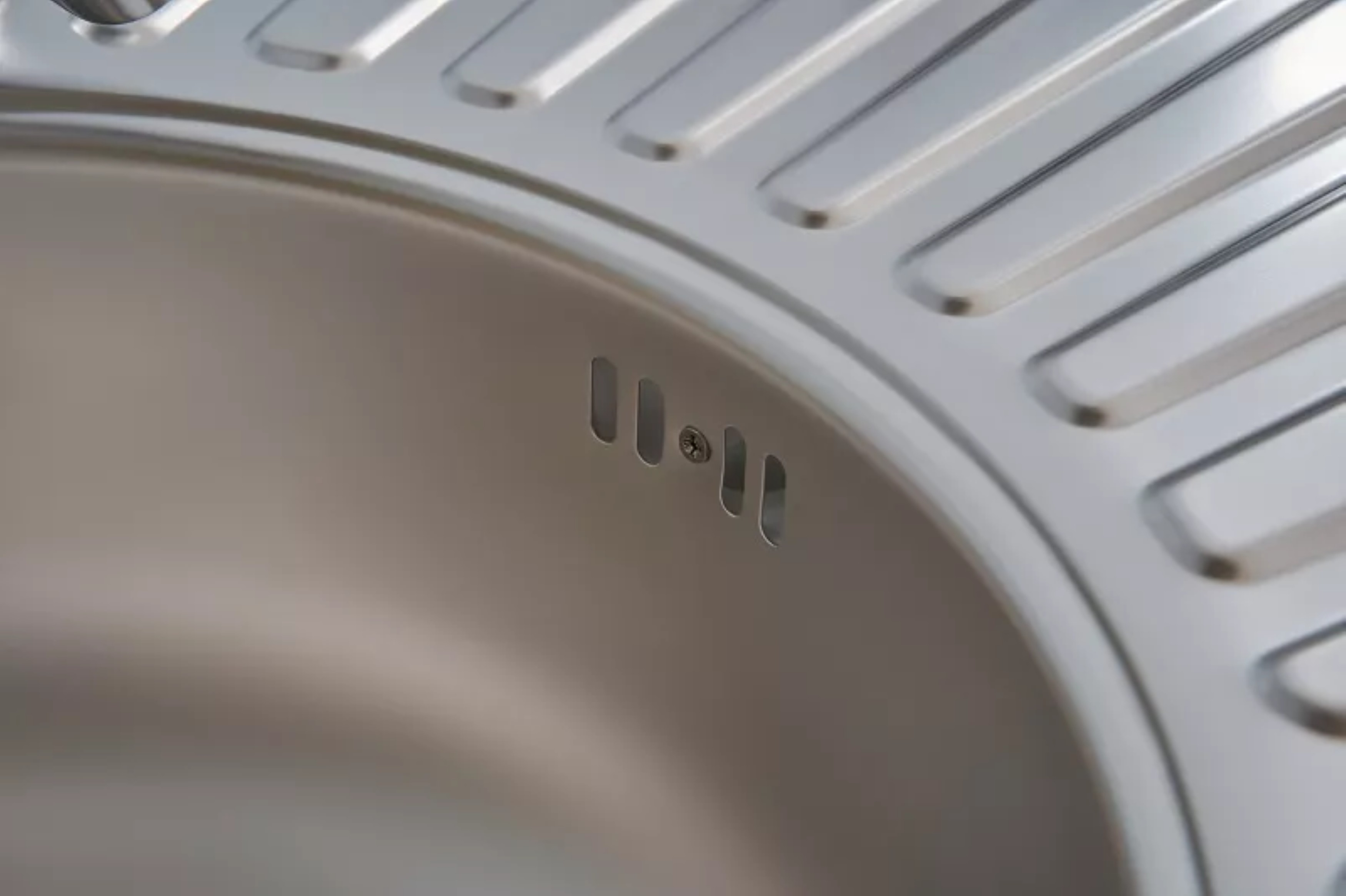 Nahaufnahme der Abflusslöcher eines Edelstahlbeckens. Das Becken hat ein gerilltes Design.