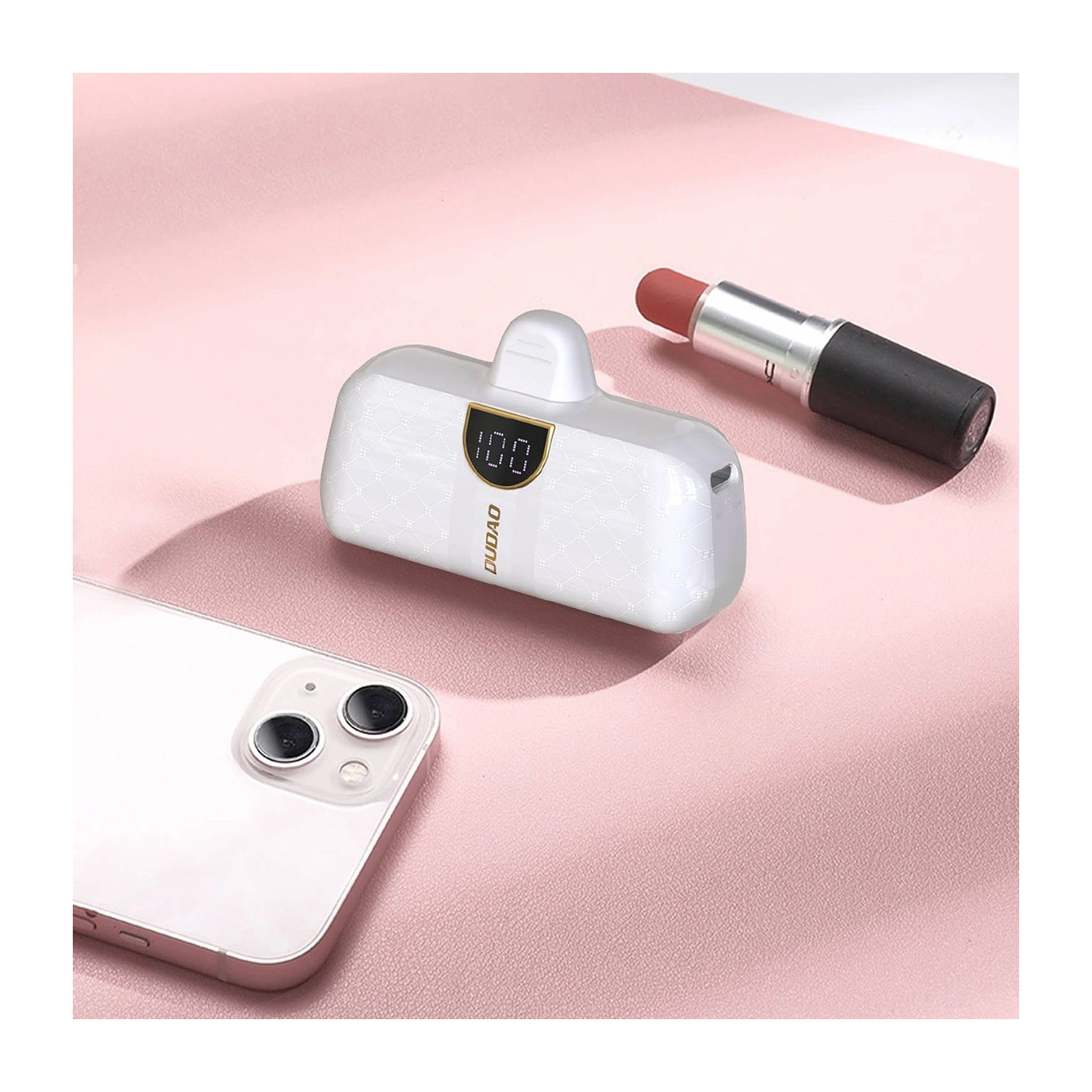 Power bank, szminka i telefon na różowej powierzchni. Power bank wyświetla 100.