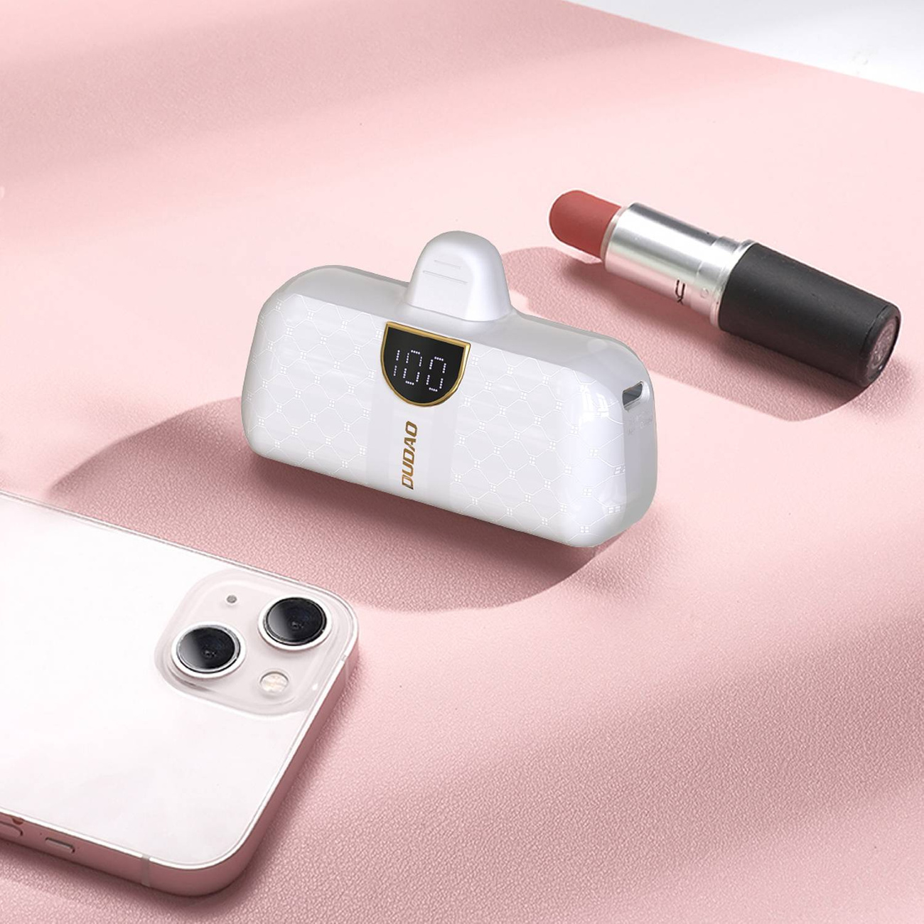 Power bank z szminką i telefonem na różowej powierzchni.