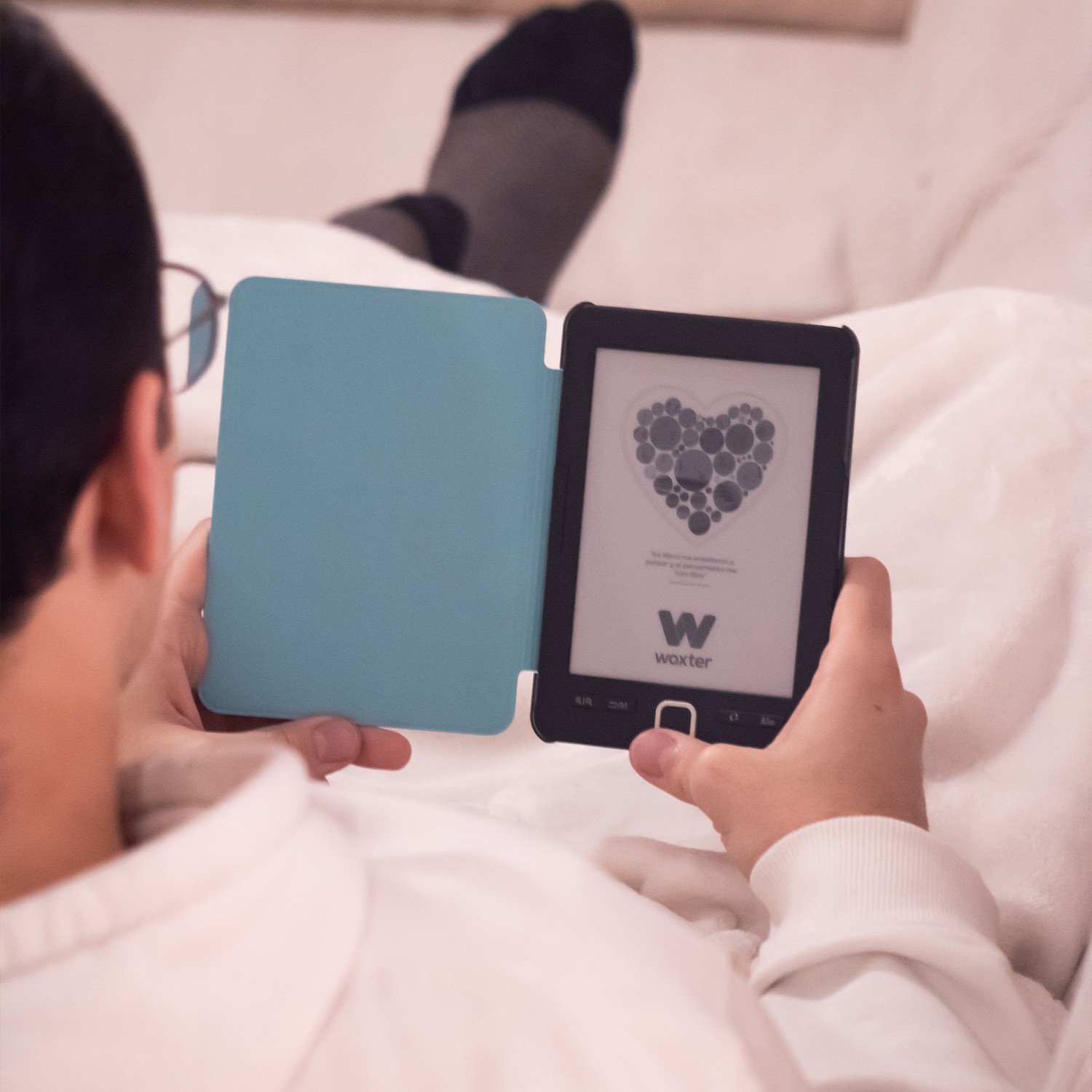 Osoba trzymająca czytnik ebooków w jasnoniebieskim etui, pokazująca wzór serca. W pomieszczeniu.