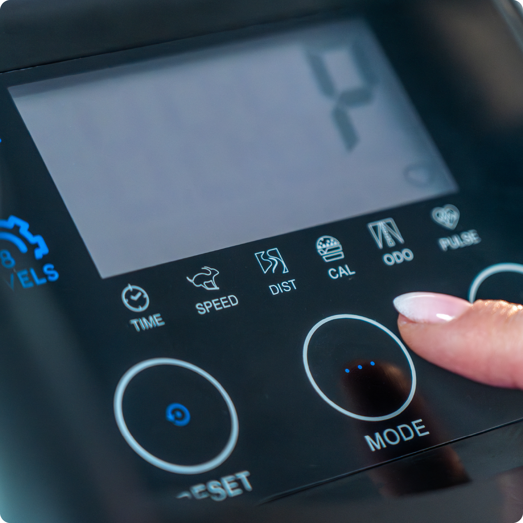 Zbliżenie panelu sterowania maszyny eliptycznej, palec naciska przycisk.