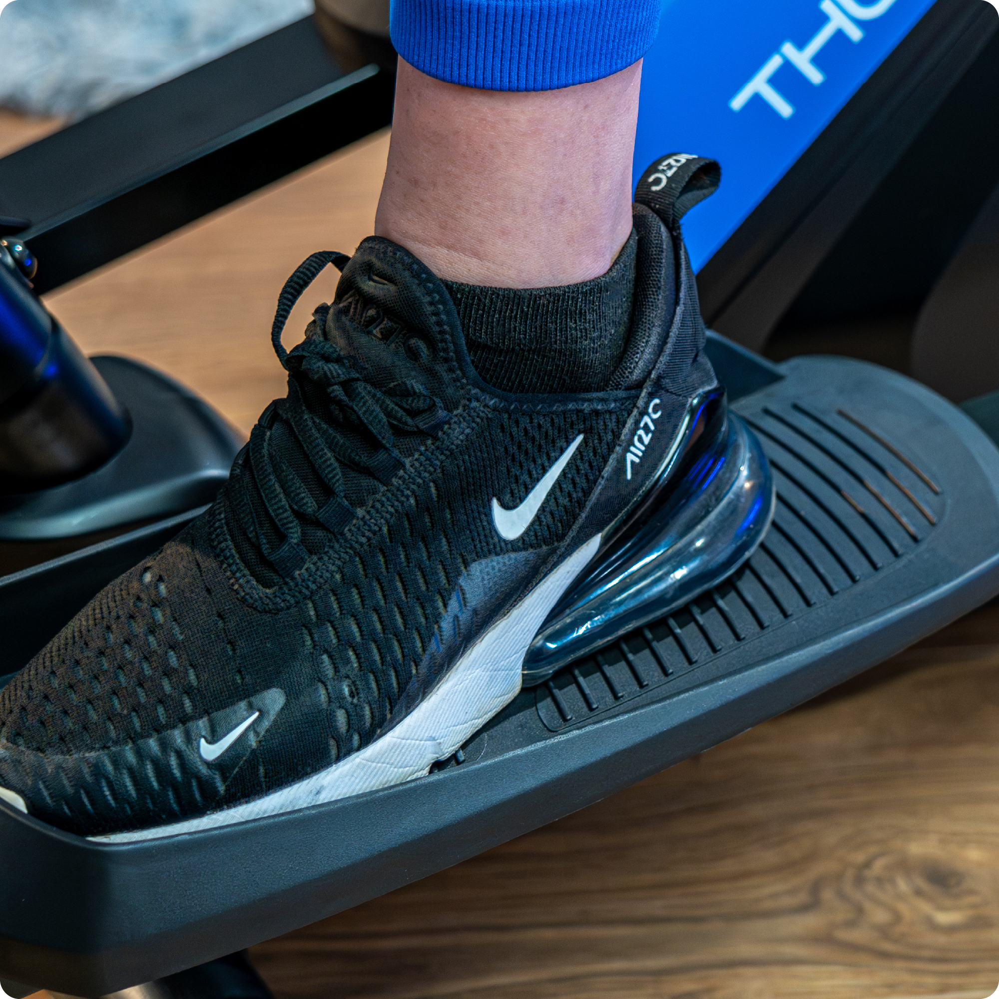 Stopa w czarnym bucie Nike na maszynie eliptycznej. Widoczne niebieskie legginsy.