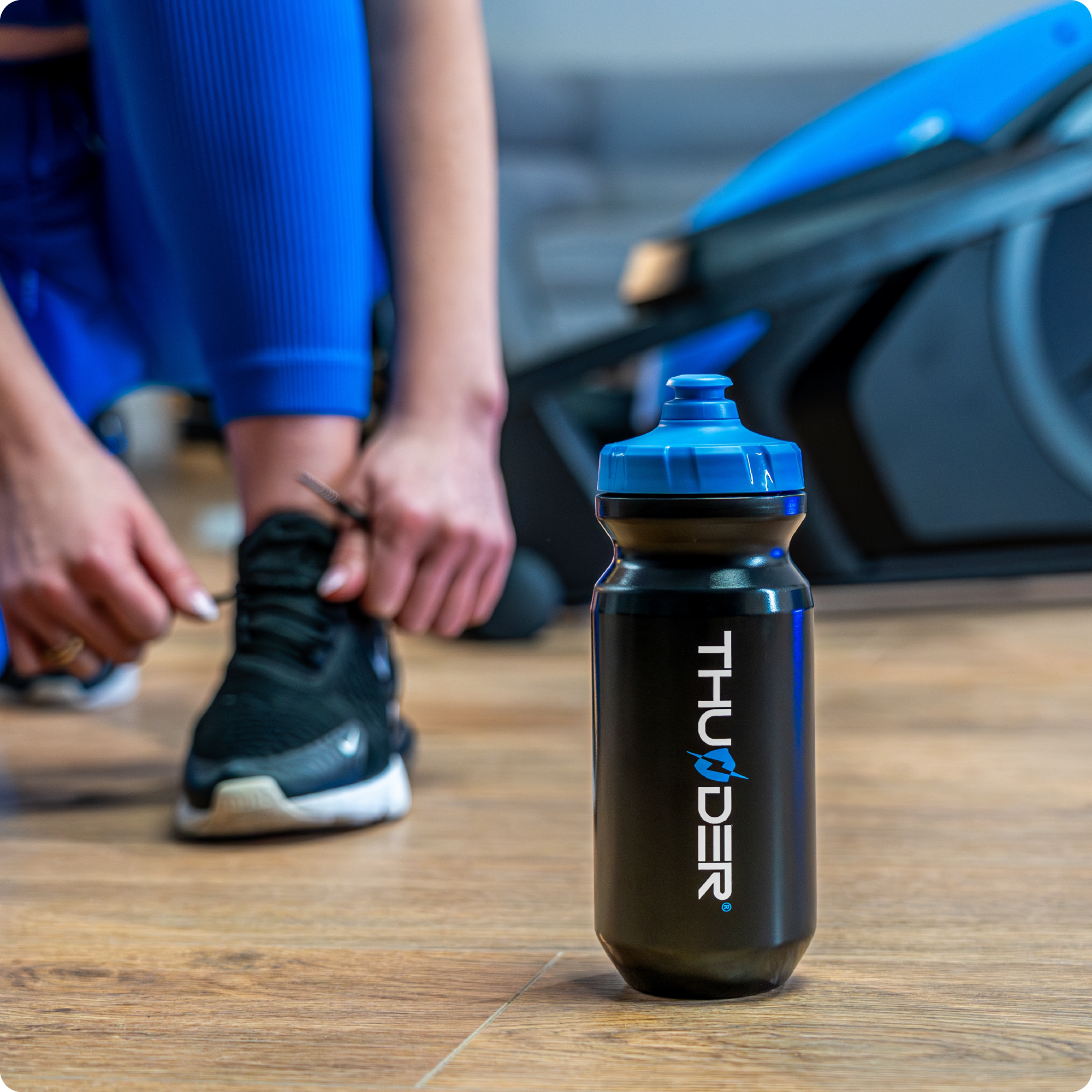 Czarna butelka z wodą i ktoś wiążący but, w tle maszyna eliptyczna.