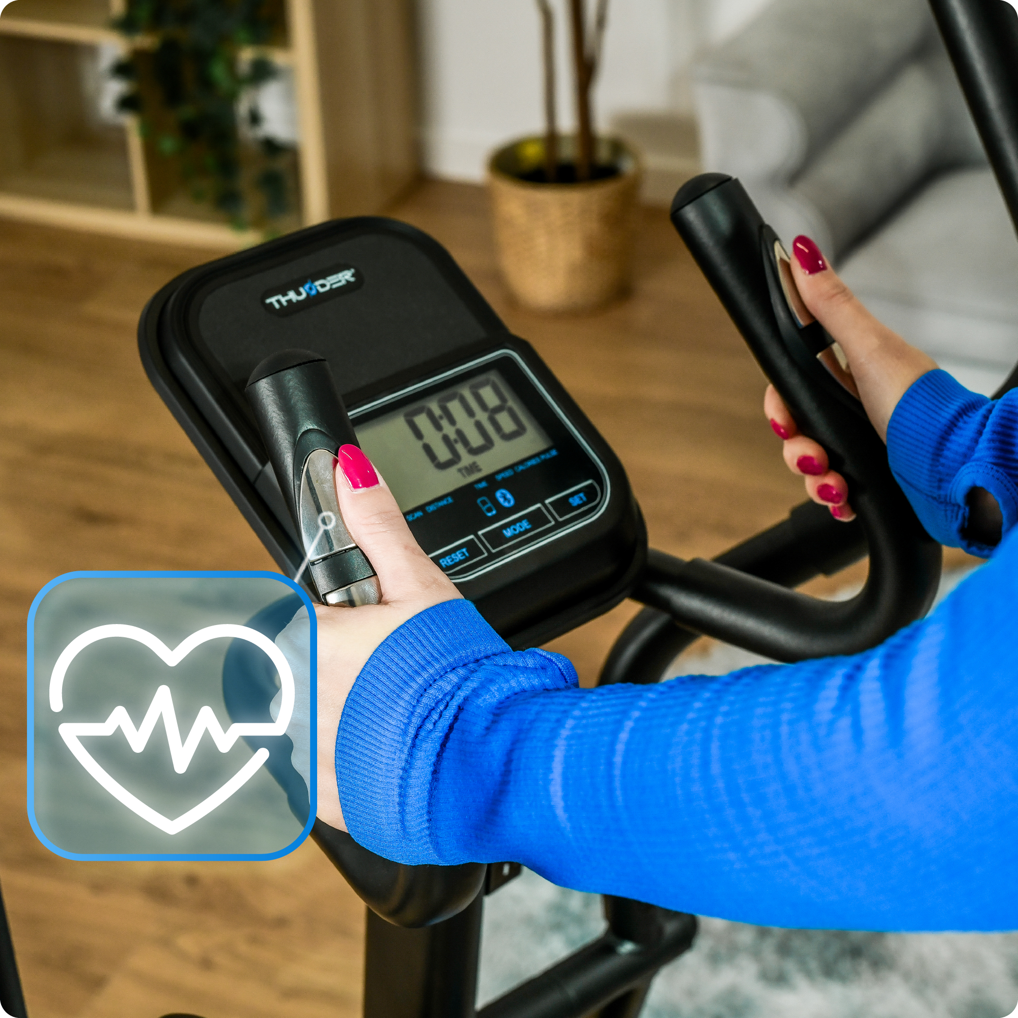 Zbliżenie wyświetlacza orbitreka. Ręce dotykają wyświetlacza. Ikona tętna jest widoczna.