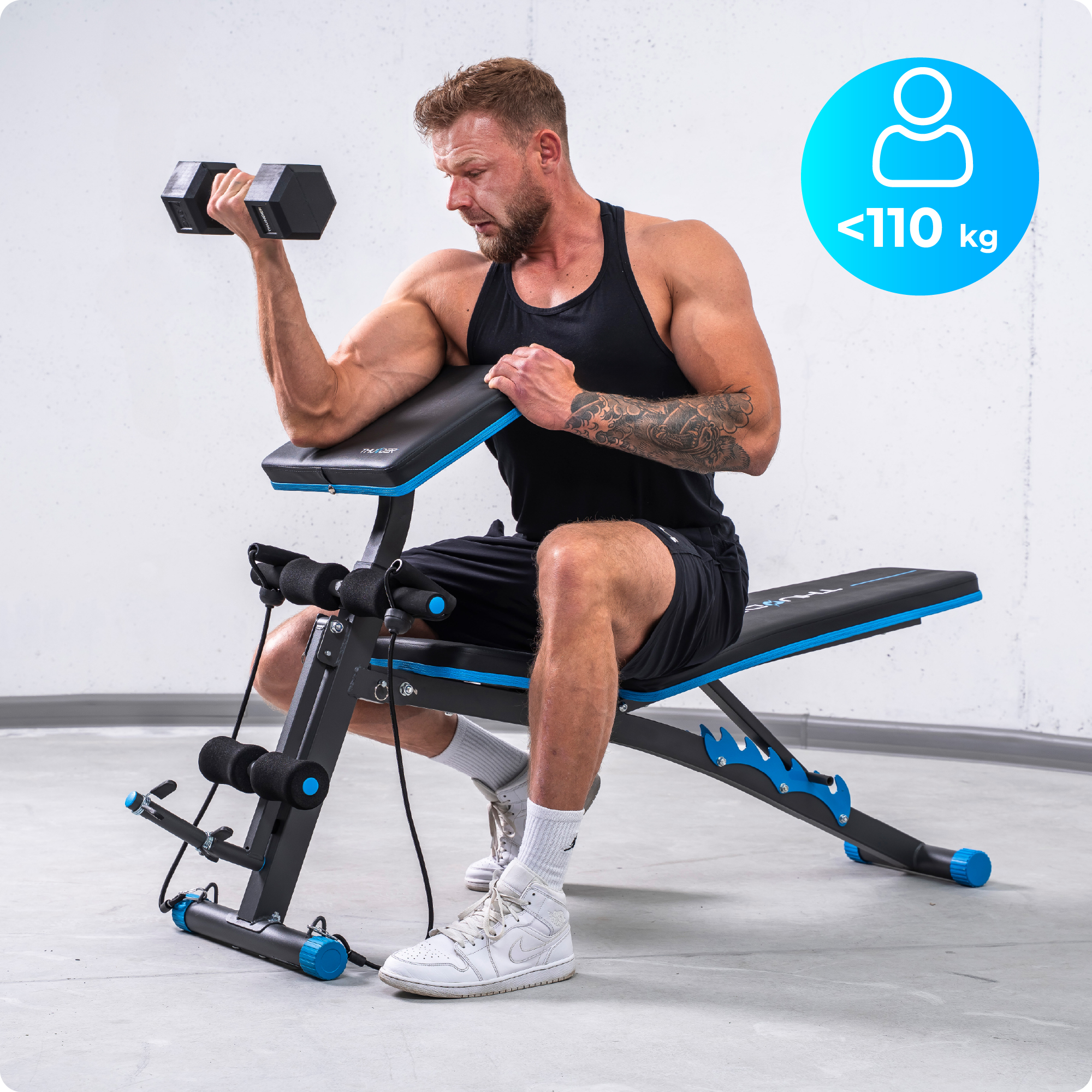 Mężczyzna podnosi hantle siedząc na ławce do ćwiczeń. Maksymalna waga <lt/>110 kg.