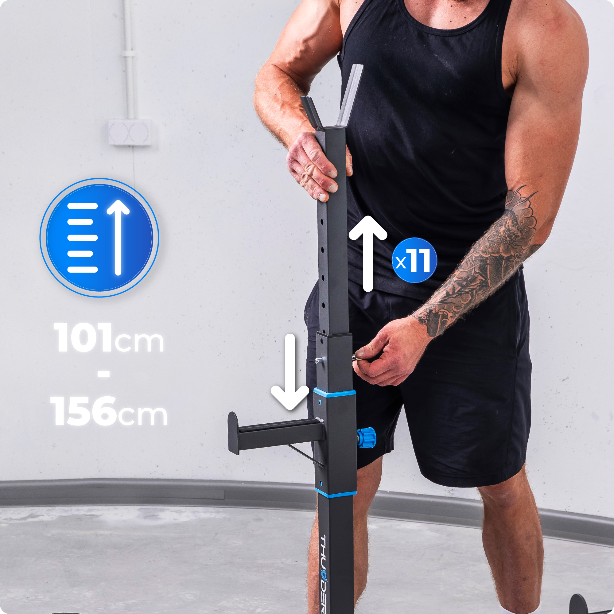 Mężczyzna reguluje czarny stojak do przysiadów z niebieskimi akcentami. Wymiary pokazane: 101cm-156cm.