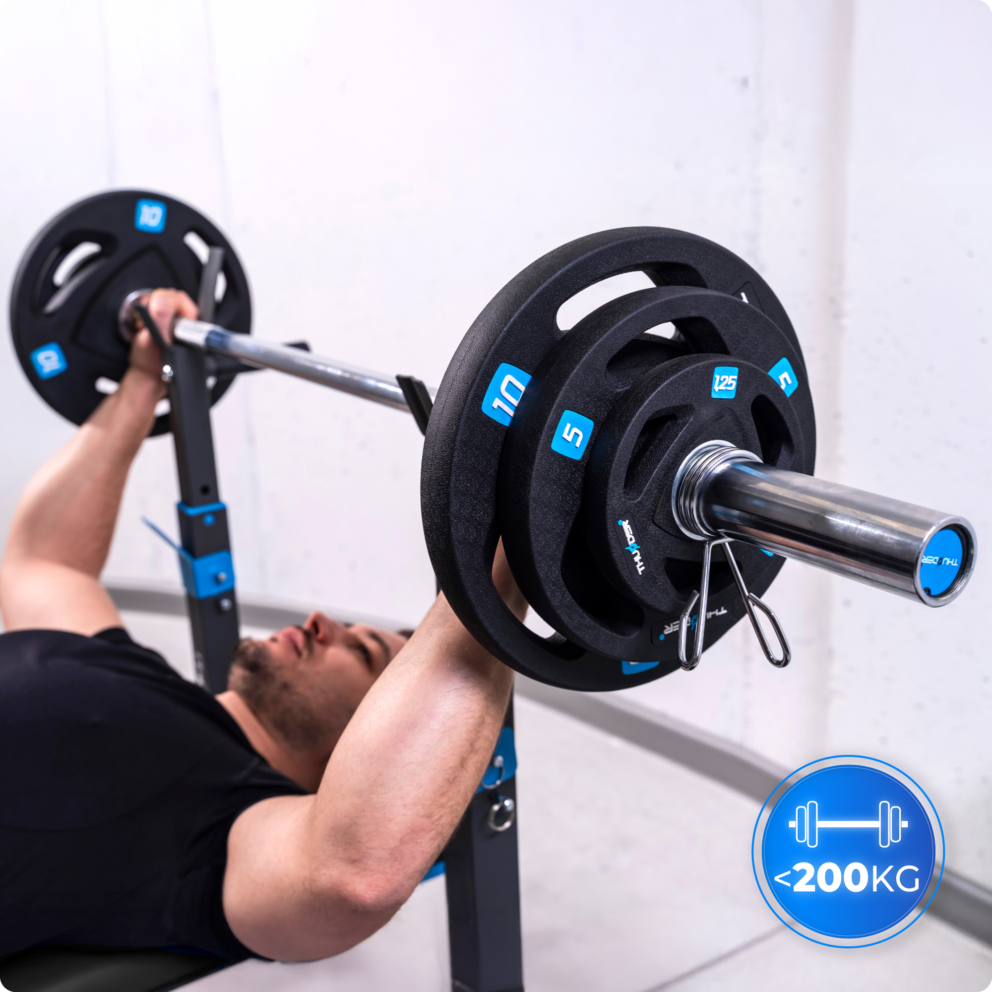 Mężczyzna wyciska sztangę na ławce z obciążeniami. Limit wagi poniżej 200 kg pokazany w rogu.