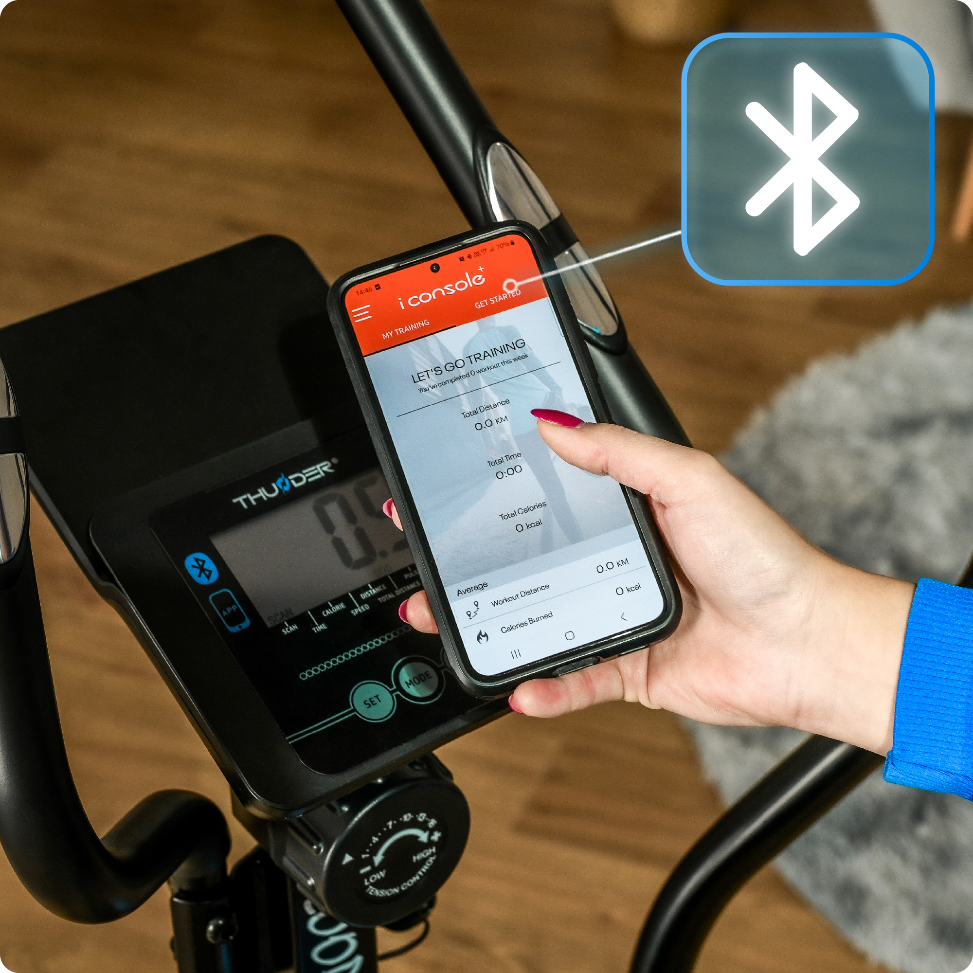 Ręka trzymająca telefon pokazujący aplikację na wyświetlaczu. Połączony z maszyną eliptyczną przez Bluetooth.
