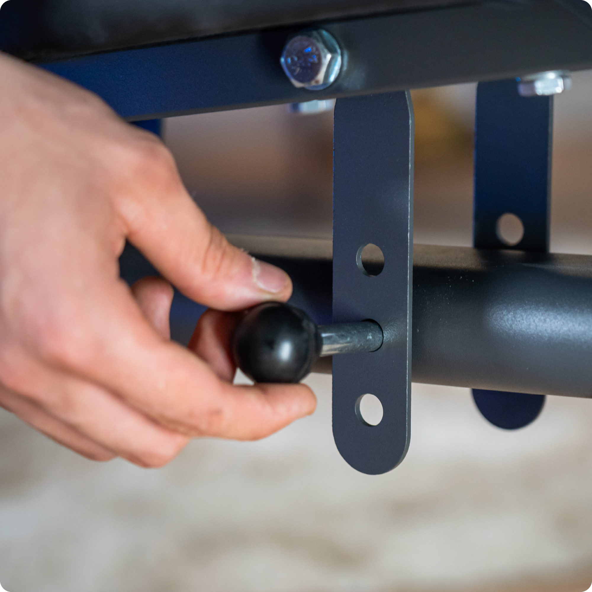 Dłoń używająca narzędzia do regulacji ławki do ćwiczeń. Ławka jest czarna i szara.