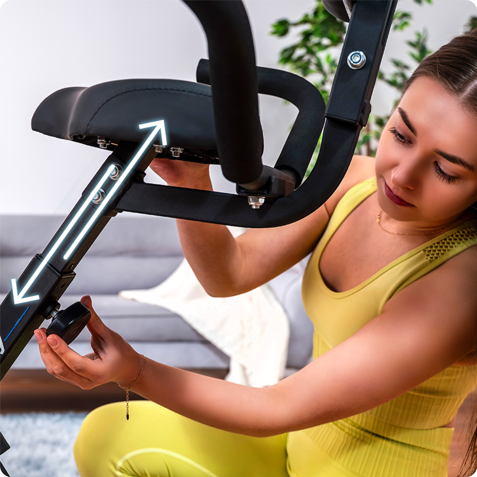 Kobieta reguluje siedzenie składanego roweru treningowego. Strzałki wskazują regulację wysokości.