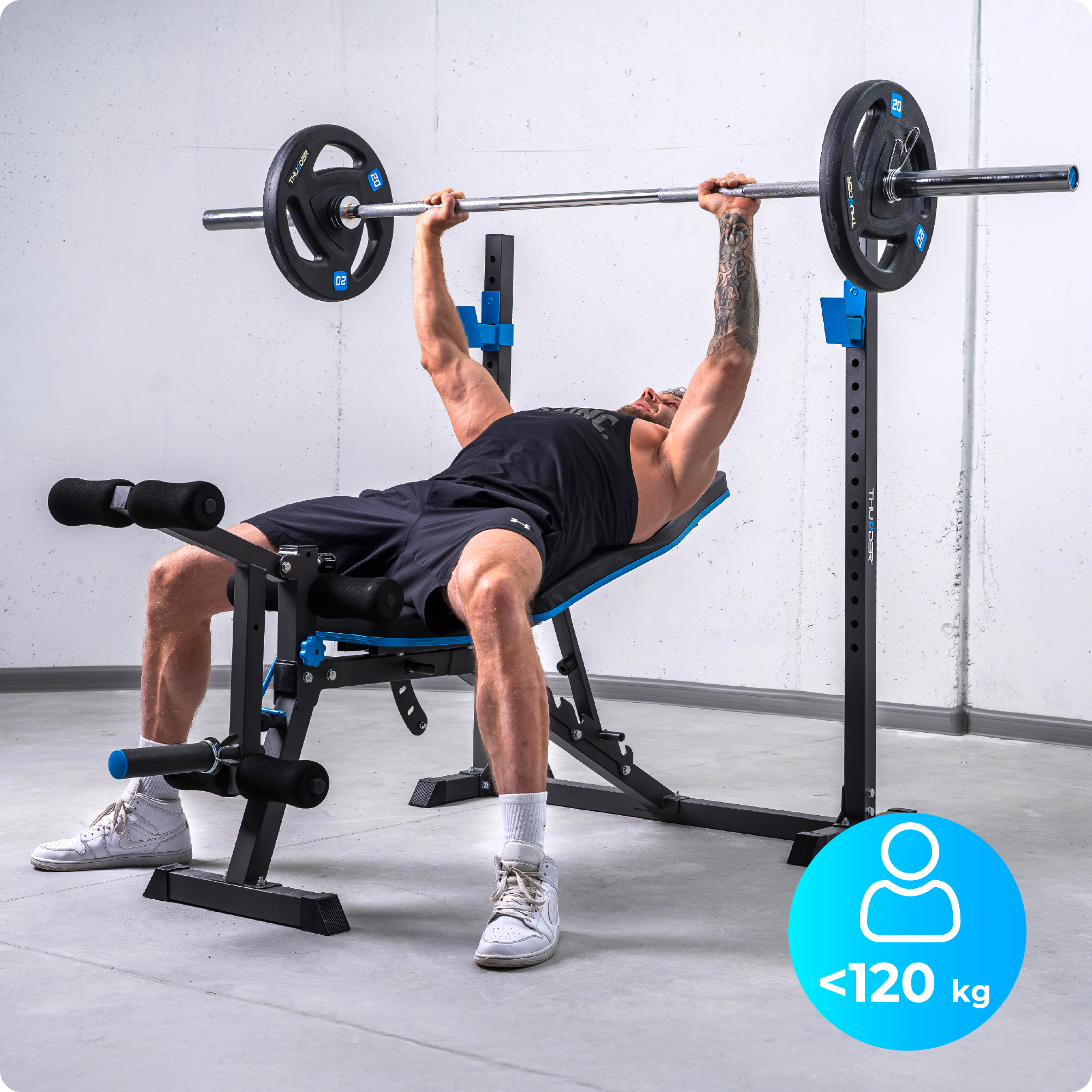 Mężczyzna wykonuje wyciskanie na ławce na ławce do ćwiczeń. Ławka jest czarno-niebieska. Mężczyzna waży poniżej 120 kg.