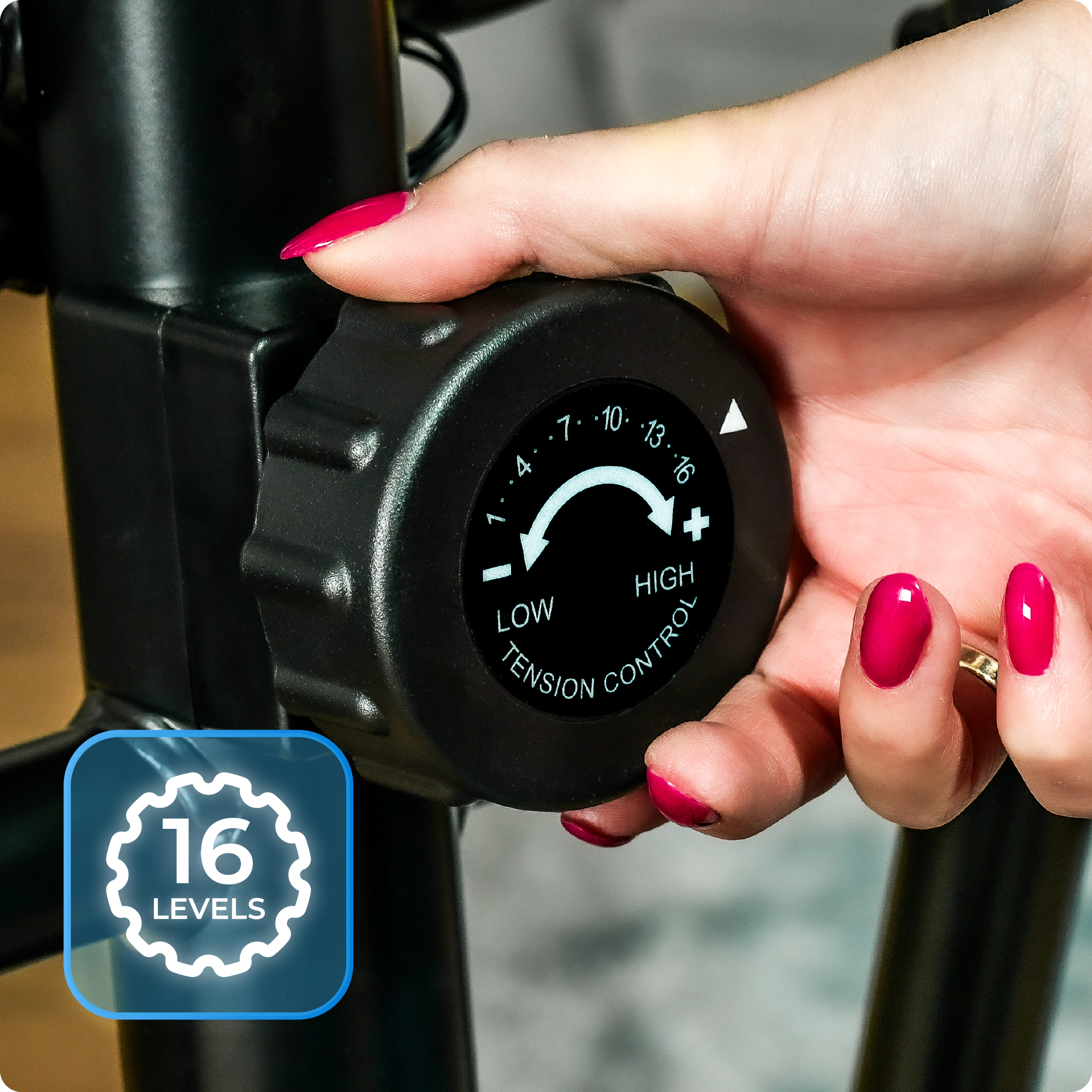 Dłoń kobiety obraca pokrętło na maszynie eliptycznej, oznaczone jako 'Tension Control', z 16 poziomami. Widoczny czerwony lakier do paznokci.
