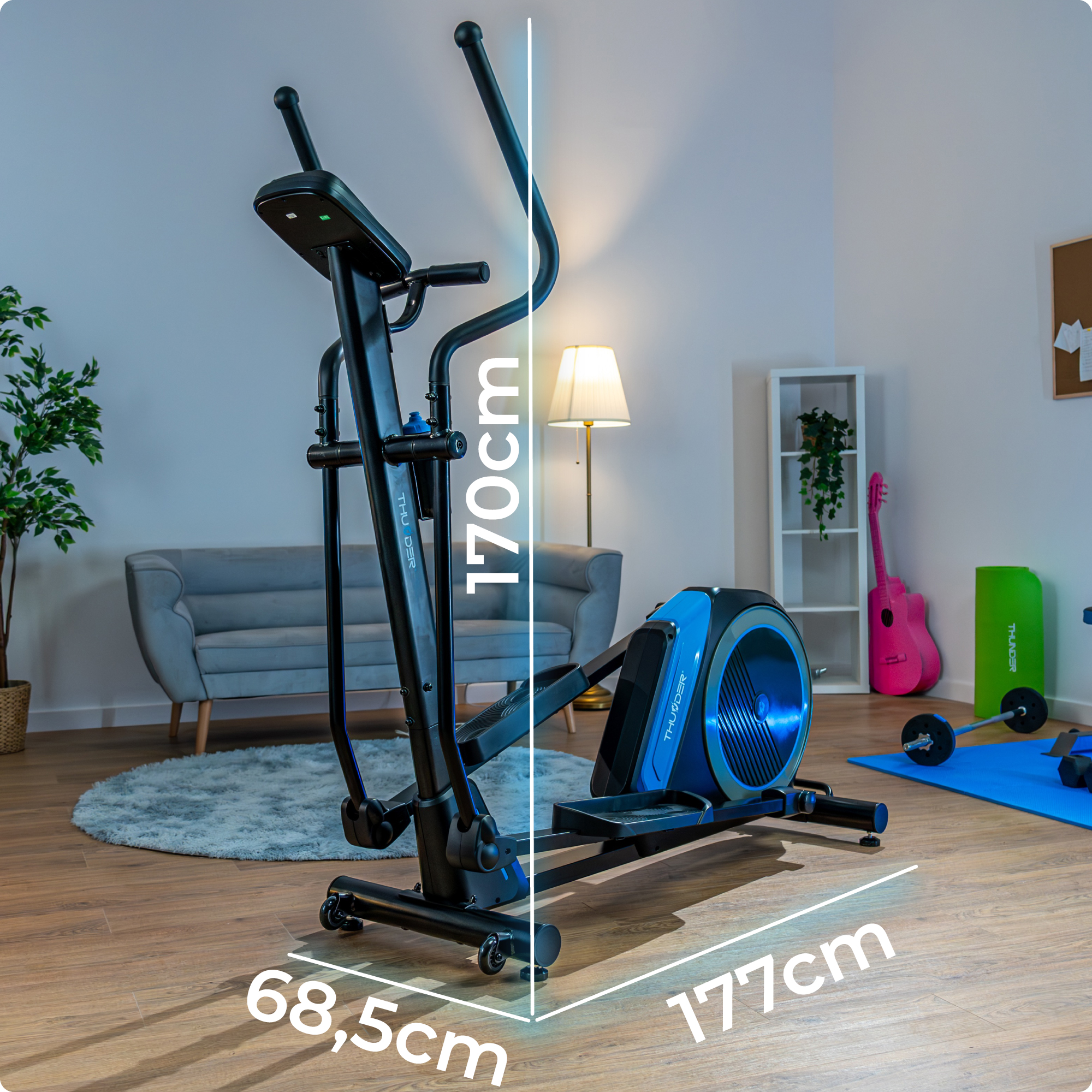 Orbitrek w pomieszczeniu z wymiarami. Jest czarno-niebieski i ma butelkę z wodą. Widoczna jest różowa gitara.