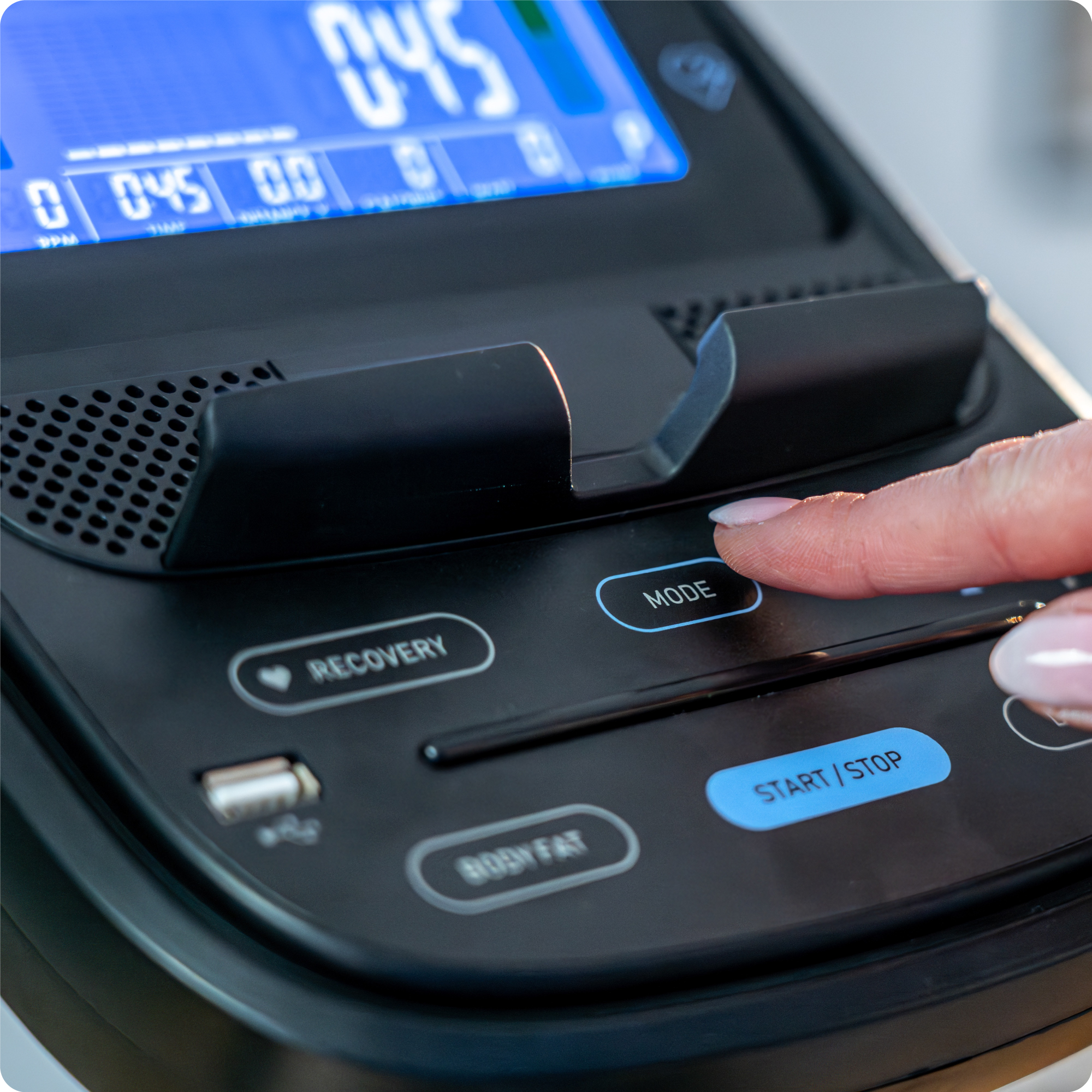 Zbliżenie panelu sterowania orbitreka. Palec naciska przycisk MODE.