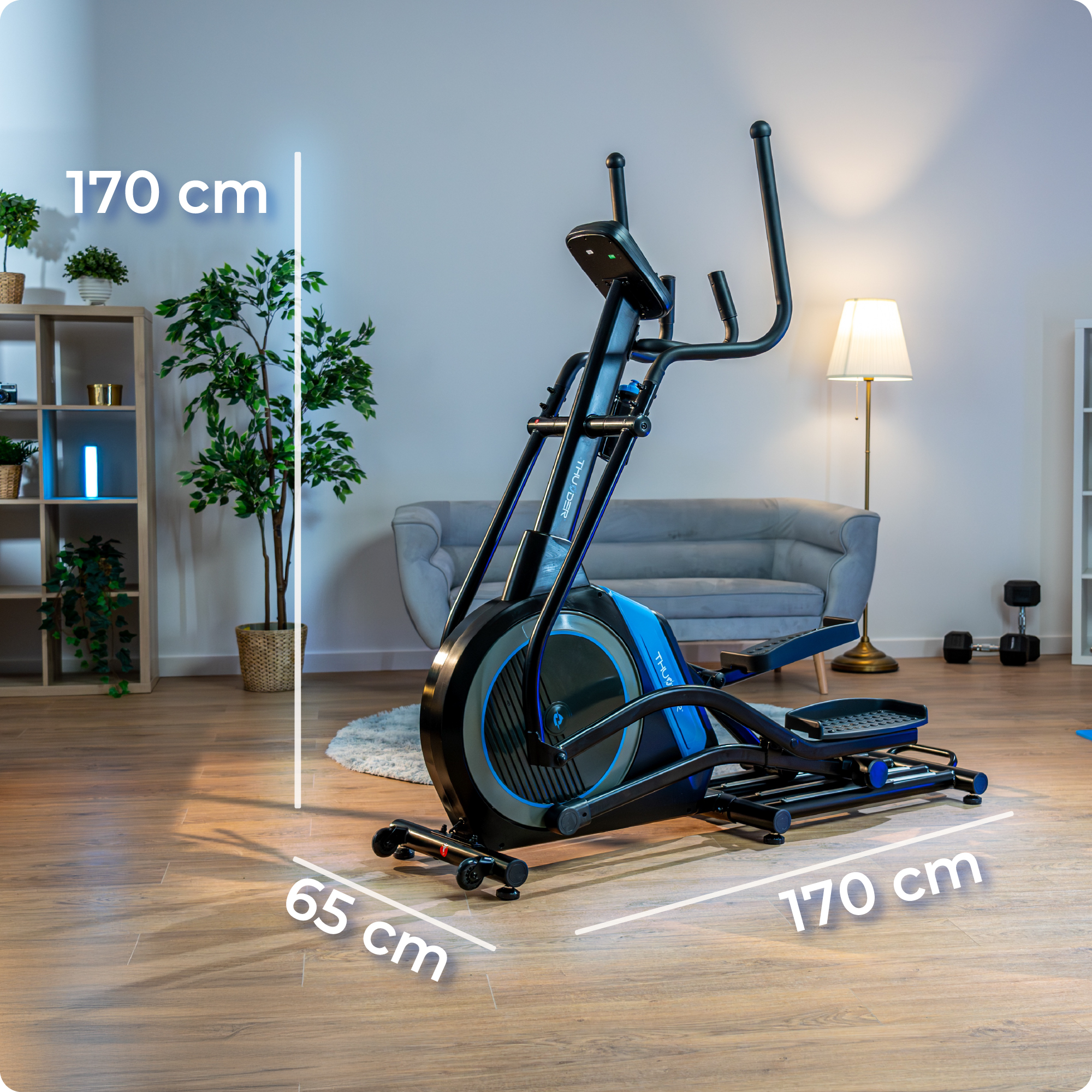 Trenażer eliptyczny w pokoju. Wymiary: 170cm x 170cm x 65cm. Rośliny, sofa i lampa widoczne w tle.