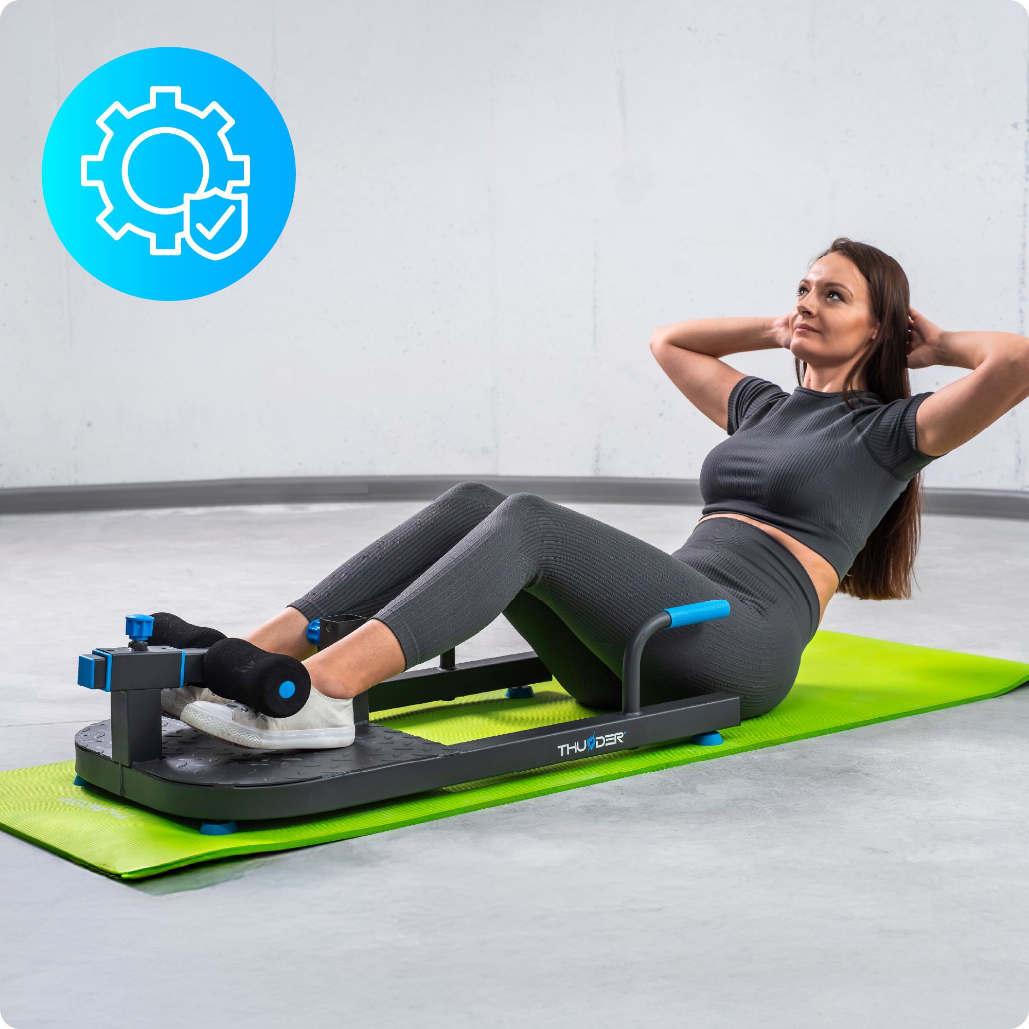 Kobieta robiąca brzuszki na zielonej macie, używając maszyny do ćwiczeń Thunder. Szare tło.