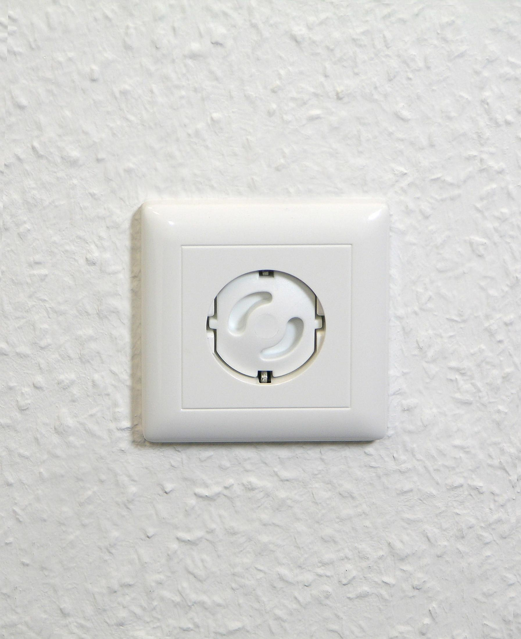 Eine weiße Steckdose mit weißer Abdeckung ist an einer strukturierten weißen Wand befestigt.