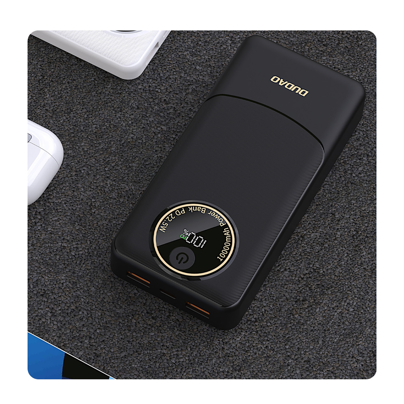 Czarny power bank DUDAO z wyświetlaczem. Pokazuje 100% naładowania. Białe etui na słuchawki w kadrze.