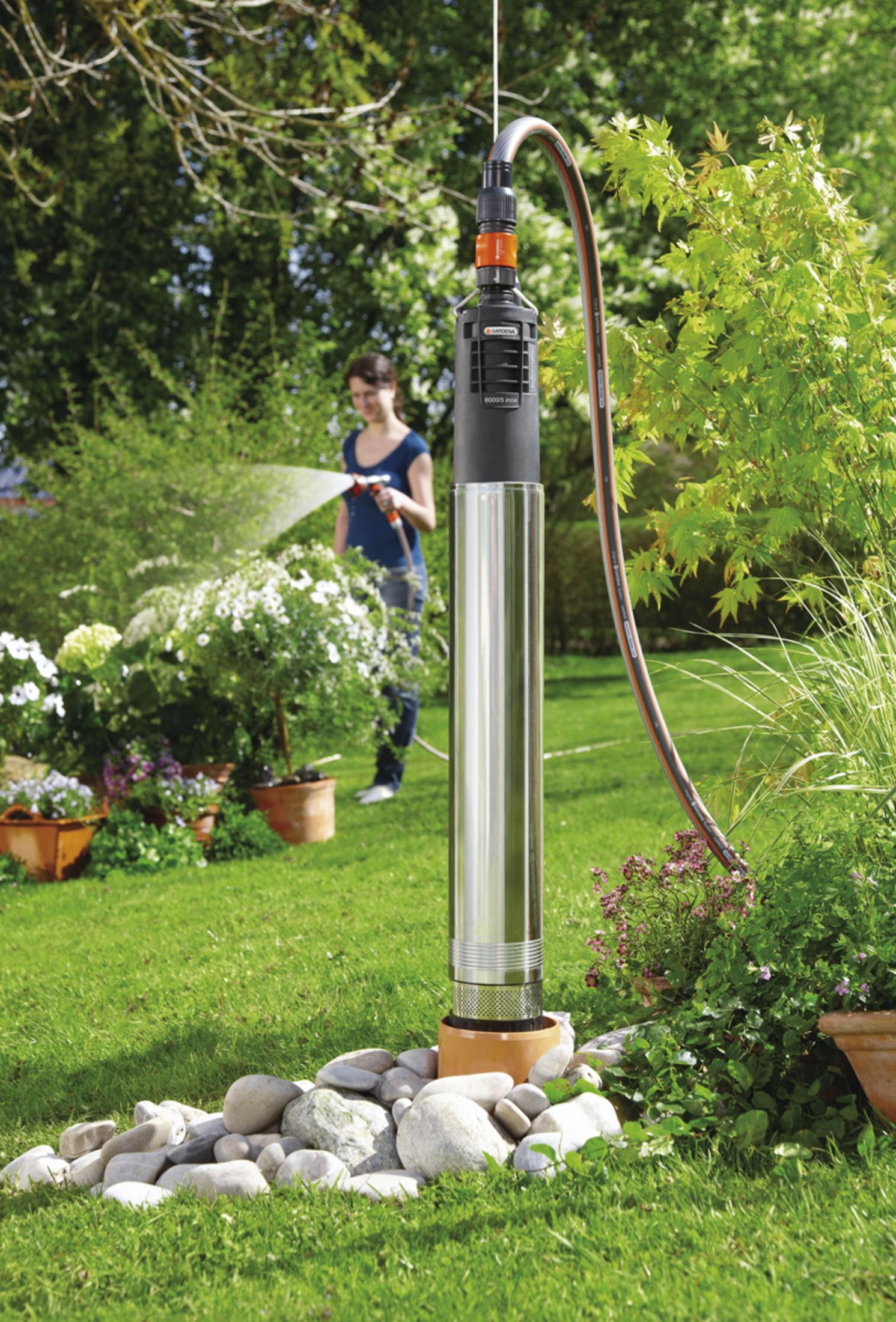 Eine Frau gießt Pflanzen in einem Garten mit einer Wasserpumpe im Vordergrund.