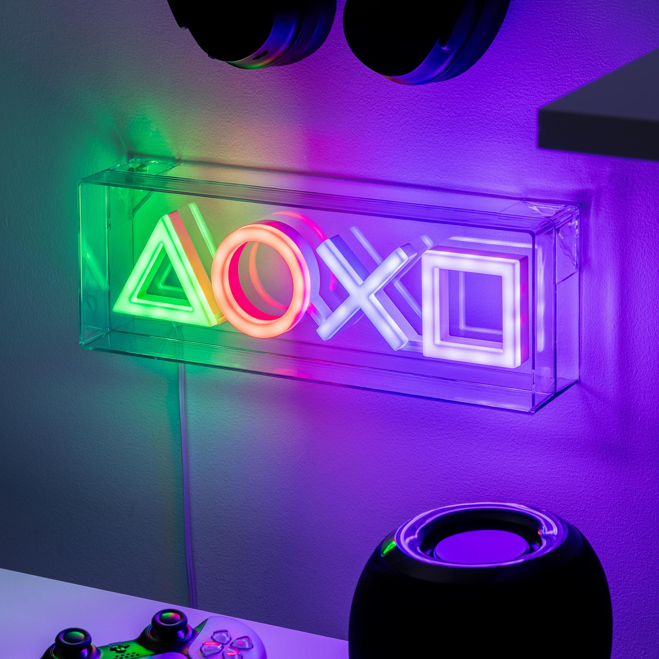 Neonowe światło PlayStation z symbolami trójkąta, koła, x i kwadratu w przezroczystej ramie. Jest zamontowane na ścianie.