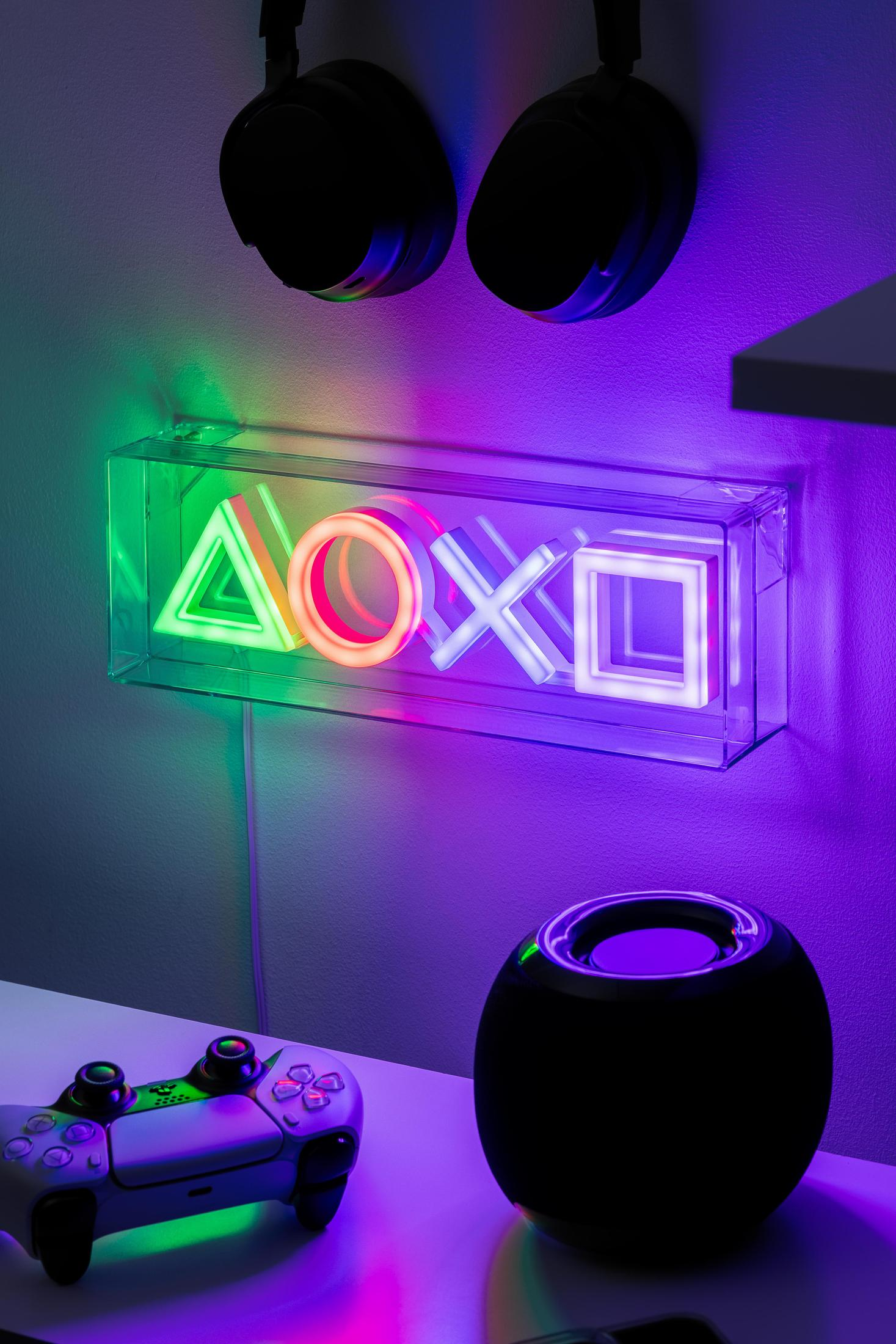 Ściana z neonowym światłem symbolu Playstation i dwoma słuchawkami wiszącymi nad kontrolerem.