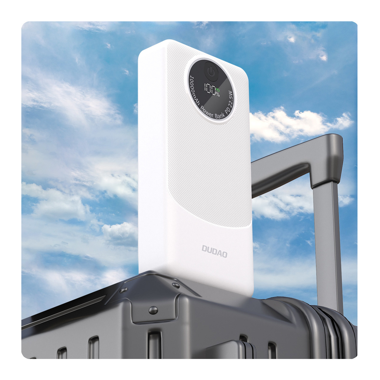 Biały power bank na czarnej walizce. Tło stanowi niebo.