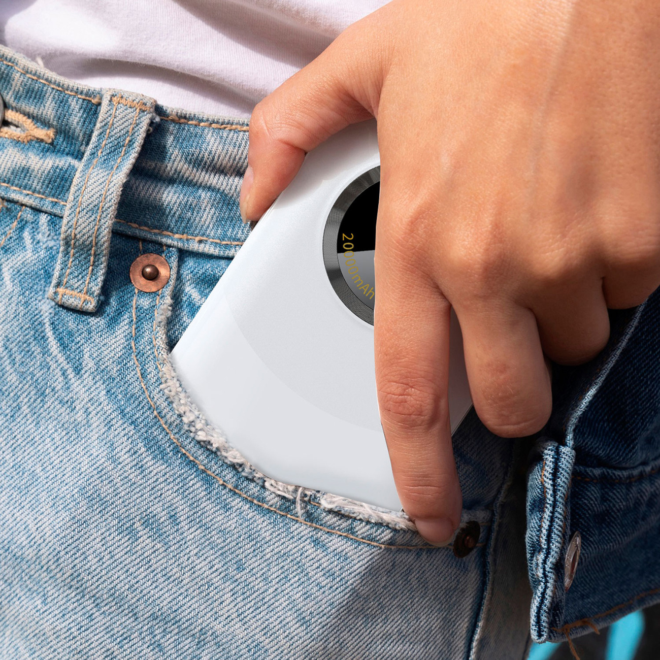 Biały power bank częściowo w kieszeni dżinsów. Bank ma pomarańczowy pasek.