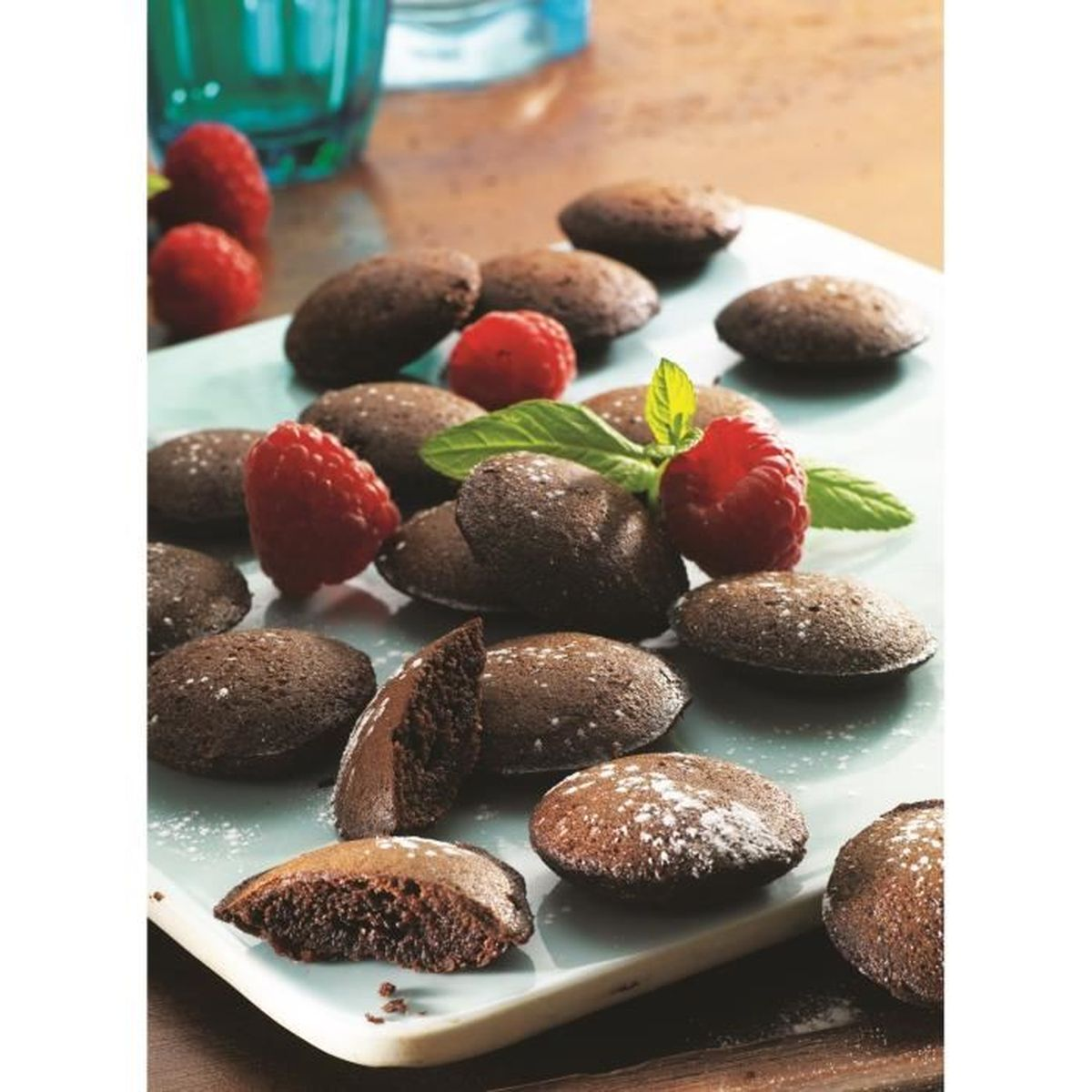 Schokoladen-Madeleines mit Himbeeren und Minzblättern auf einem Teller. Mit Puderzucker bestäubt.