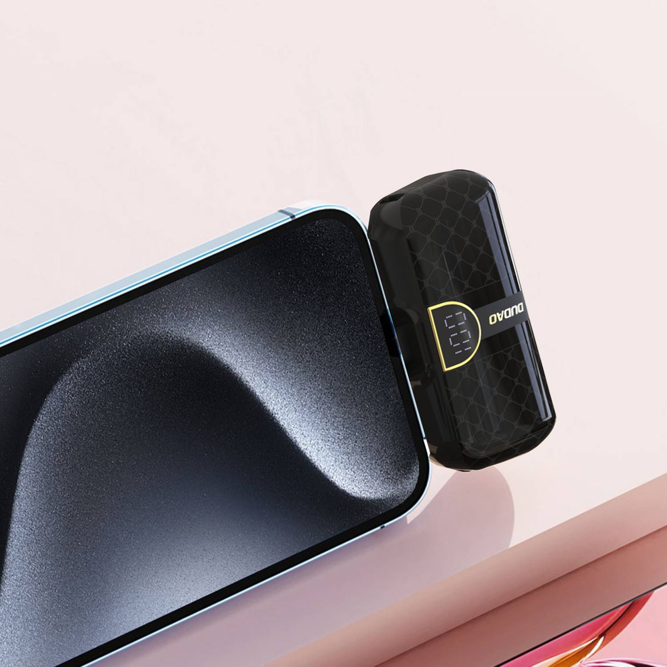 Telefon z czarnym ekranem i małą czarną ładowarką, na różowej powierzchni.