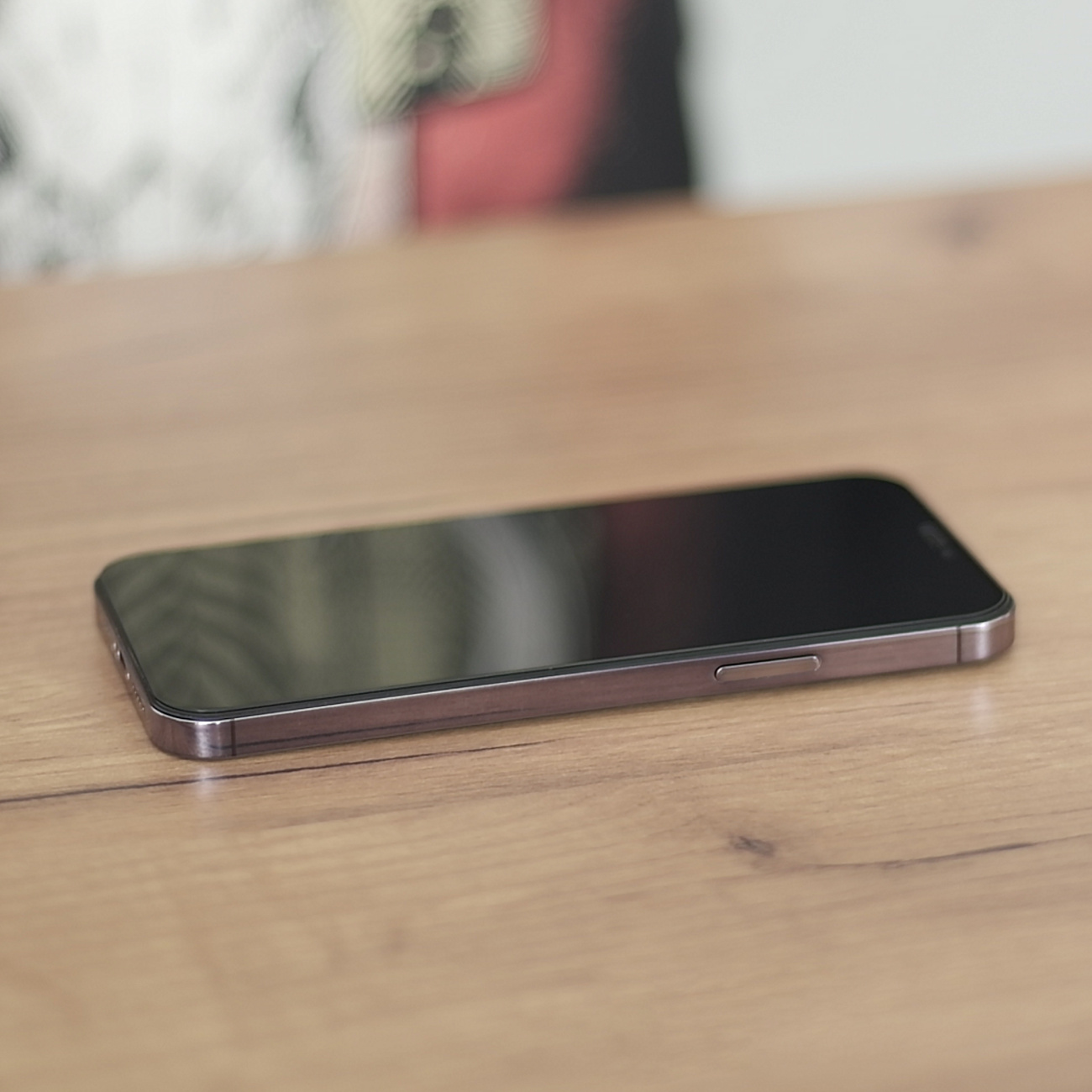 Smartfon leży na drewnianym stole. Telefon jest czarny, z metalową ramką.