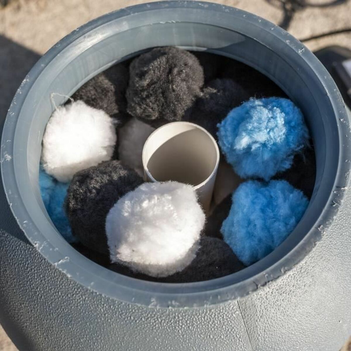 Ein grauer Behälter mit verschiedenfarbigen, flauschigen Kugeln darin. Die Kugeln sind blau, weiß und schwarz.