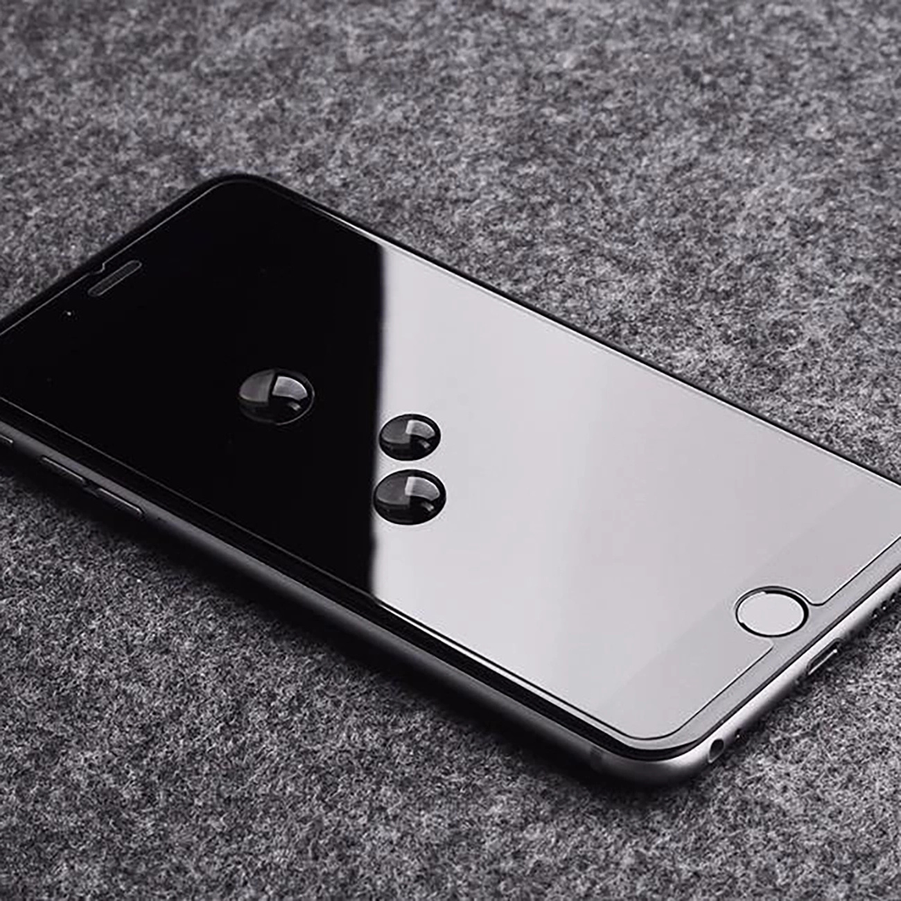 Czarny smartfon z kroplami wody na szarej powierzchni. Ekran odbija otoczenie.