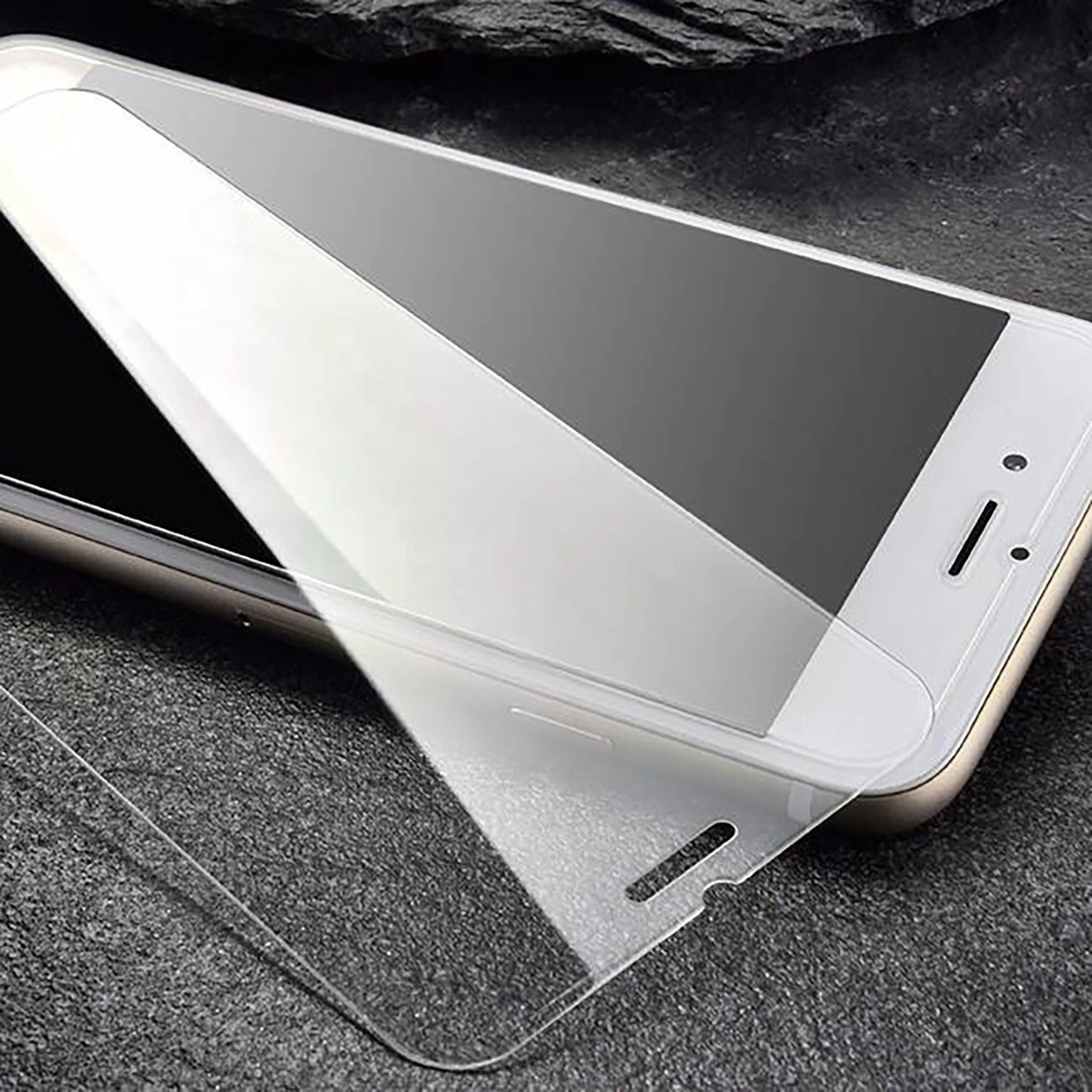 Telefon z nakładanym ochraniaczem ekranu, lekko pochylony na szarej powierzchni.
