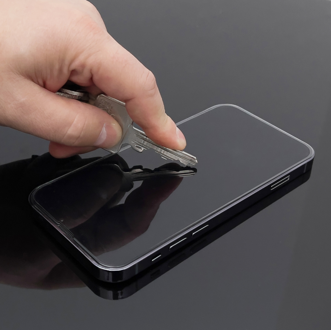 Ręka kładzie klucz na smartfonie. Telefon jest czarny, odbija powierzchnię.