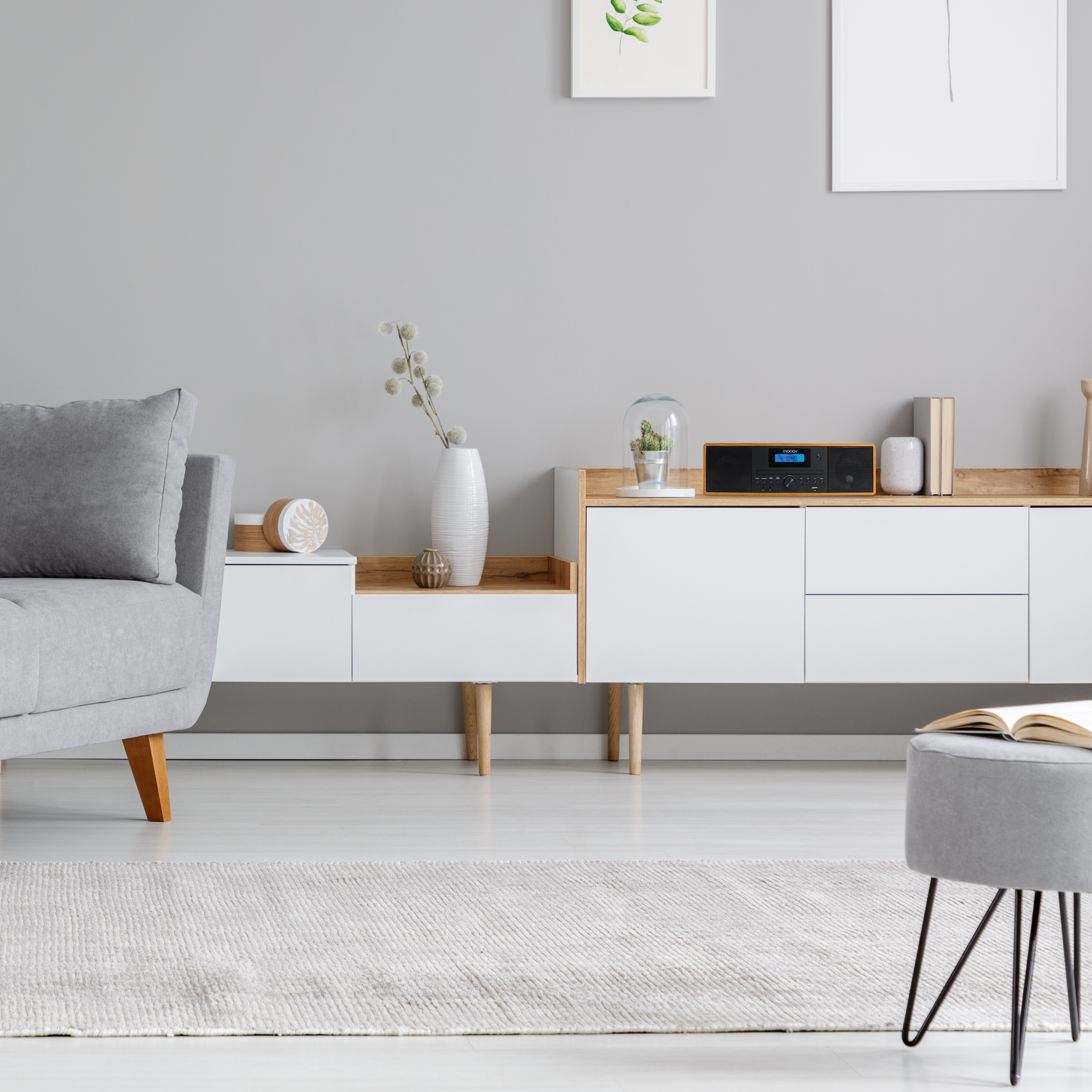 Salón con sofá gris, mueble blanco y alfombra gris. Una radio está sobre el mueble.