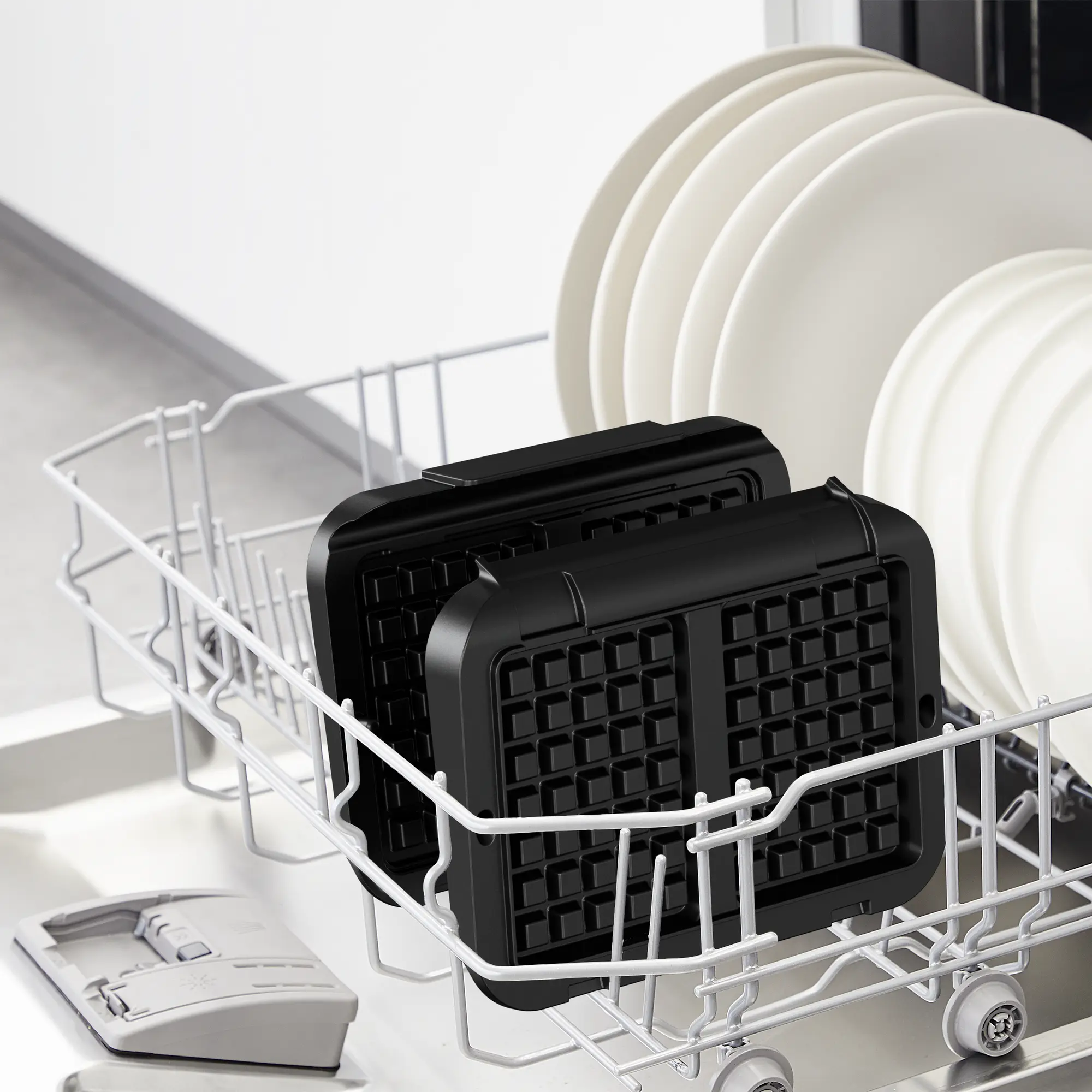 Zmywarka z płytami do gofrów w koszu i białymi talerzami.