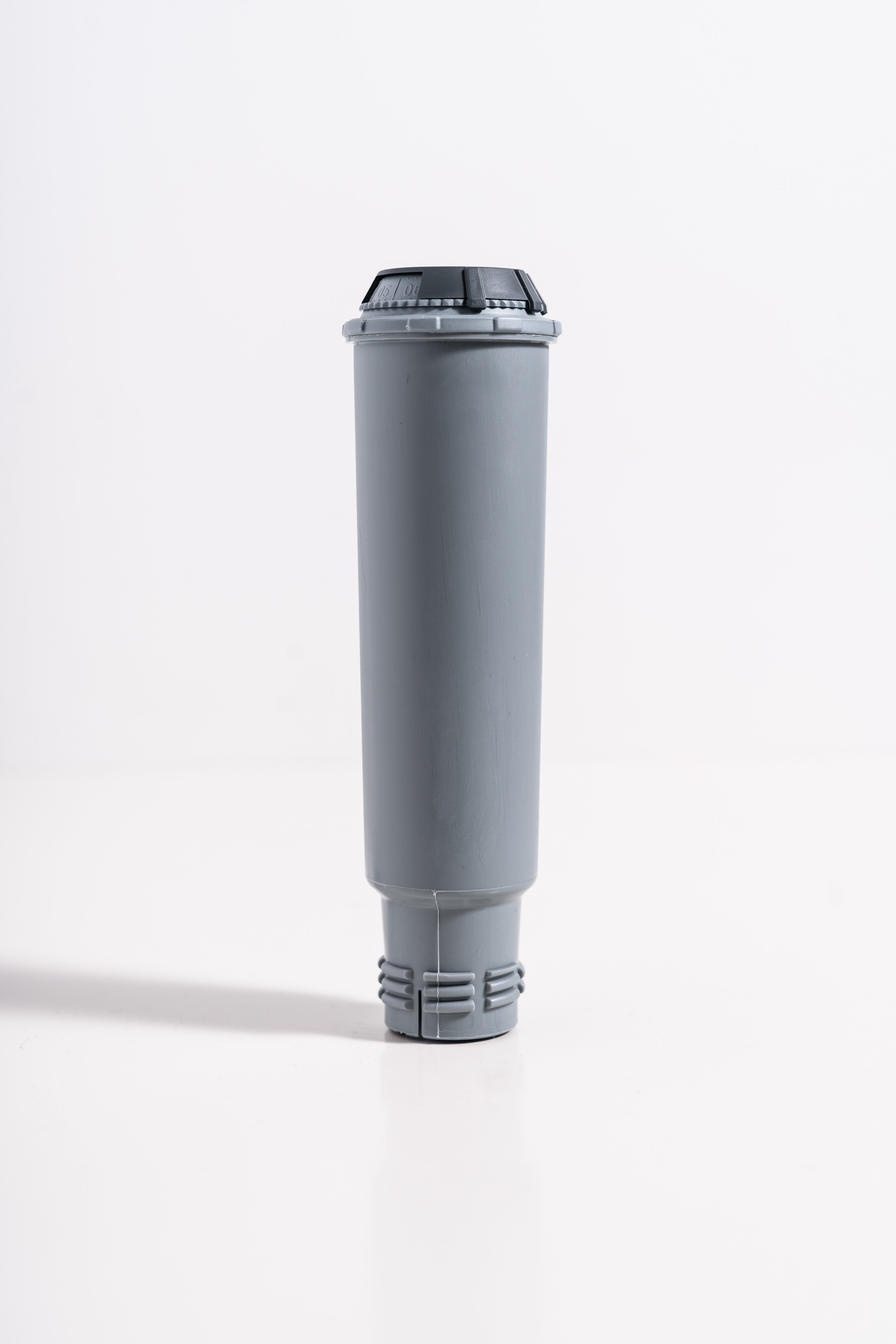 Un filtro dell'acqua grigio con la parte superiore nera, in piedi su sfondo bianco.