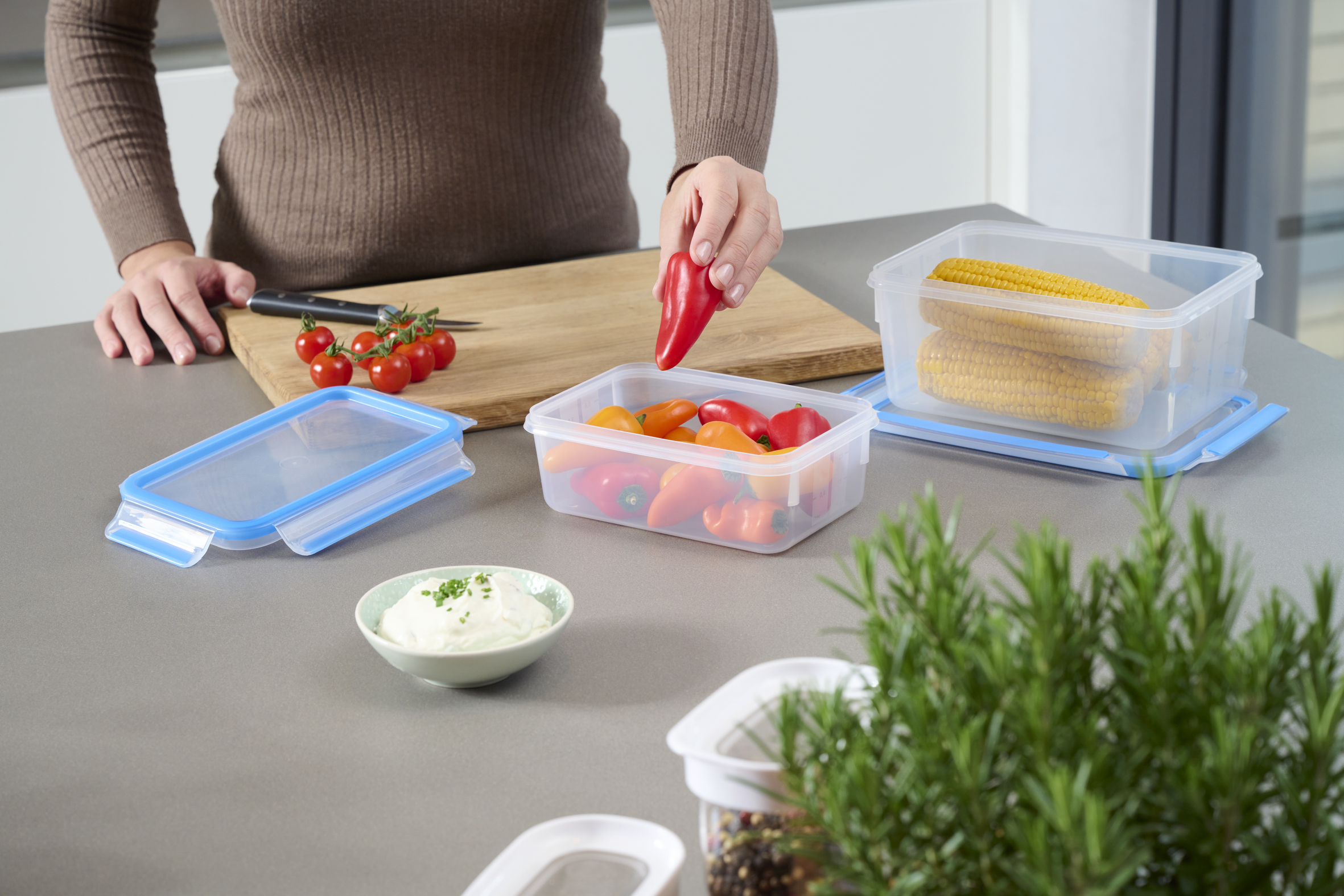 Una persona organiza verduras en recipientes en una encimera de cocina, incluyendo pimientos rojos.