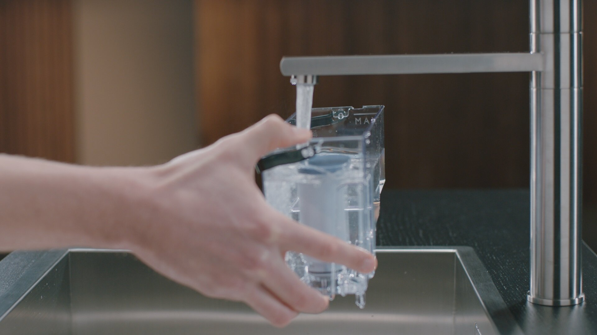 Eine Hand hält einen Wasserfilter unter einen Wasserhahn. Wasser fließt in den Filter.