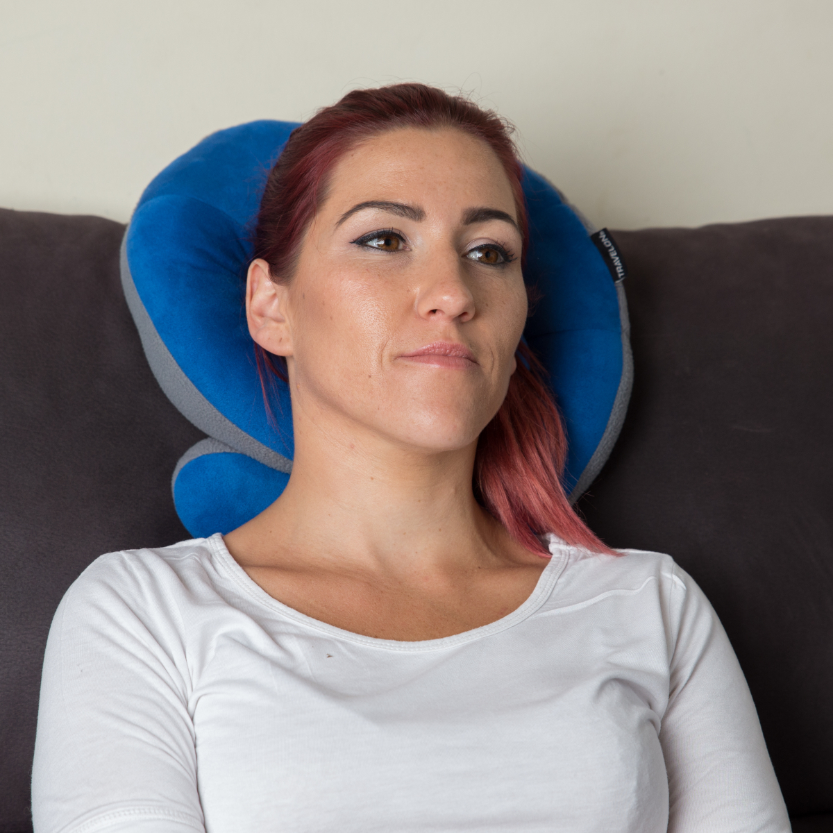 Una mujer lleva una almohada de cuello azul y gris. Tiene el pelo rosa-rojo y mira hacia un lado.