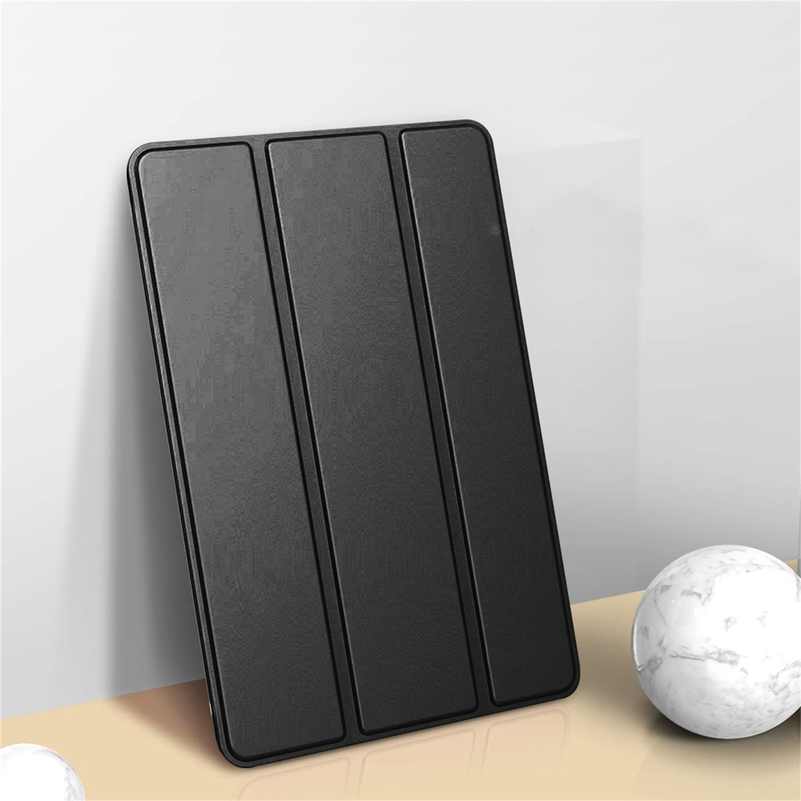 Schwarze Tablet-Hülle, die sich an einer weißen Wand anlehnt, mit drei vertikalen Paneelen. Eine Marmorkugel im Hintergrund.