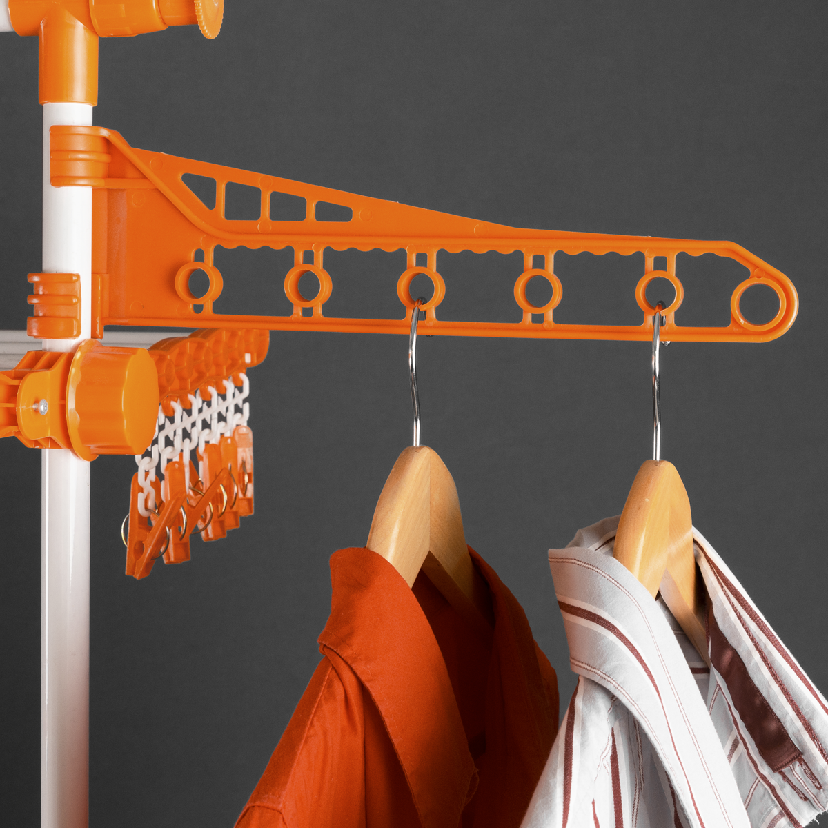 Un tendedero naranja con ropa colgada. Se ve una camisa y una camisa a rayas. Fondo gris.
